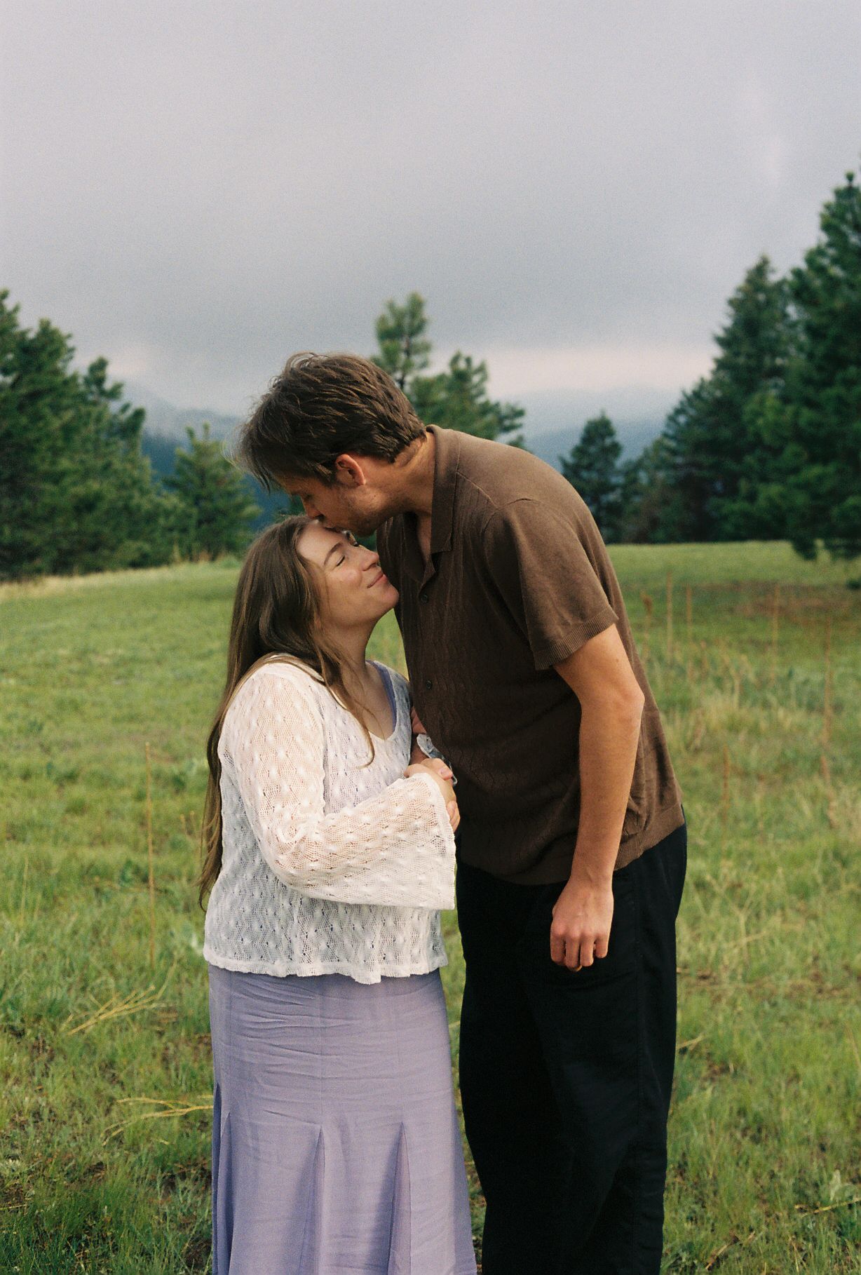 Couple sharing tender moment in green meadow with man kissing womans forehead.