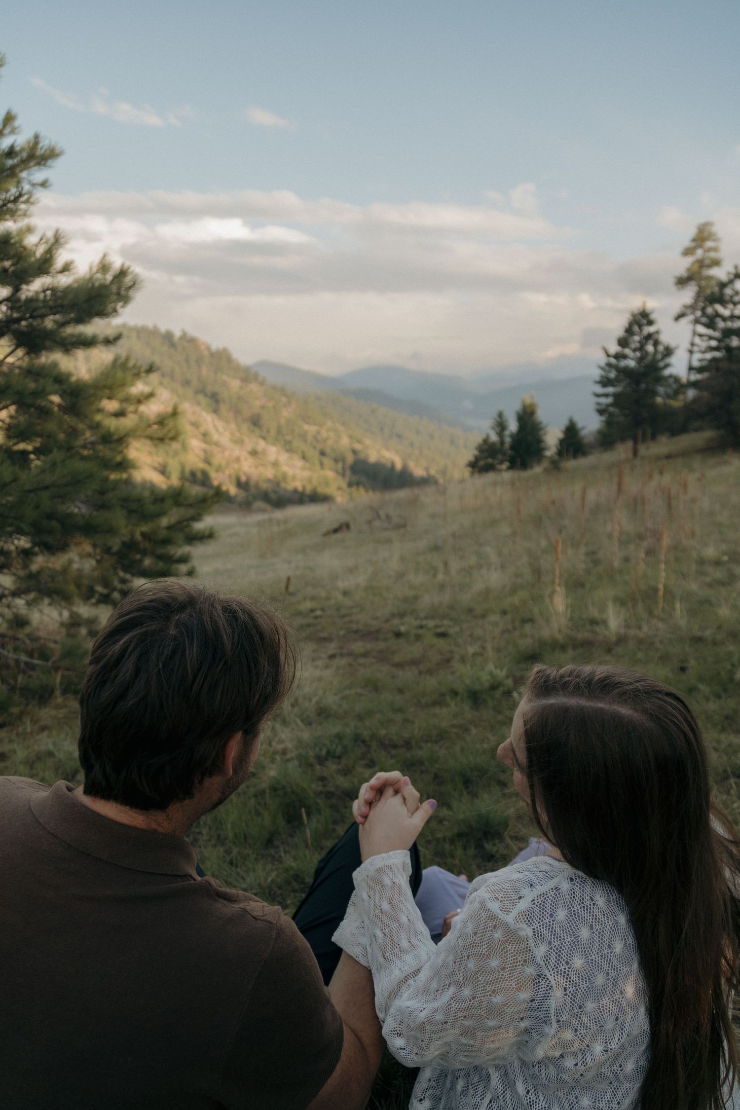 A couple holds hands while sitting together overlooking a beautiful mountain landscape.