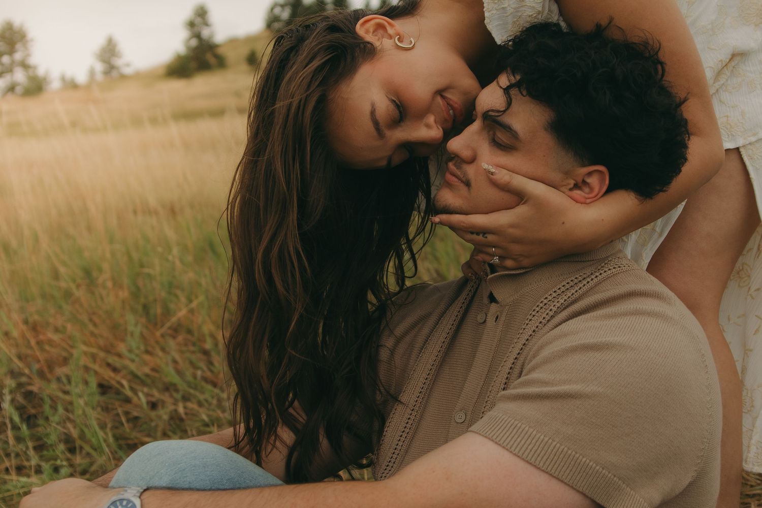 Couple sharing tender forehead touch moment while sitting in golden grass field together.