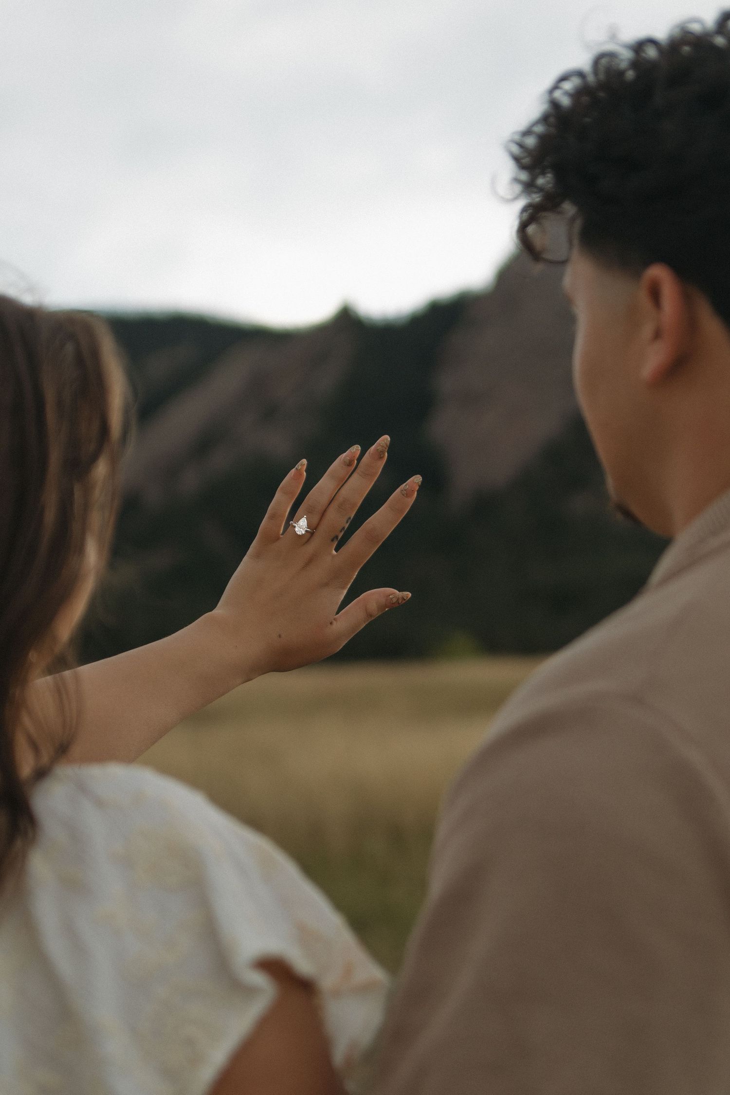 Close-up of an engagement ring on a womans hand with rocky mountain landscape in the background.