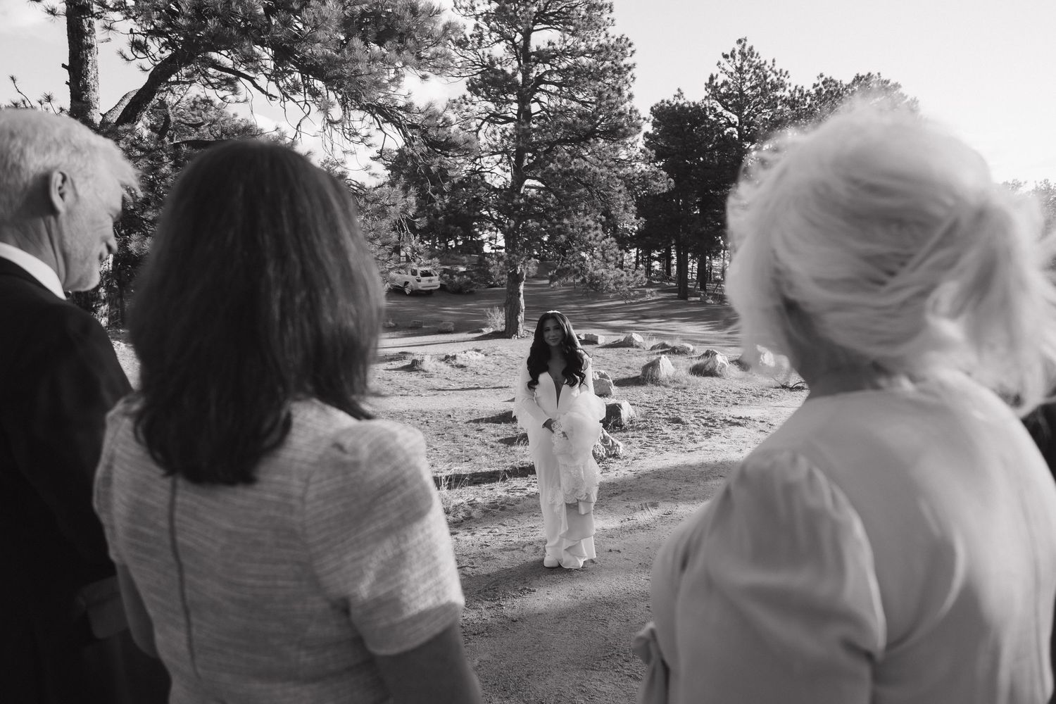 Black and white photo of wedding guests watching bride walk down outdoor aisle.