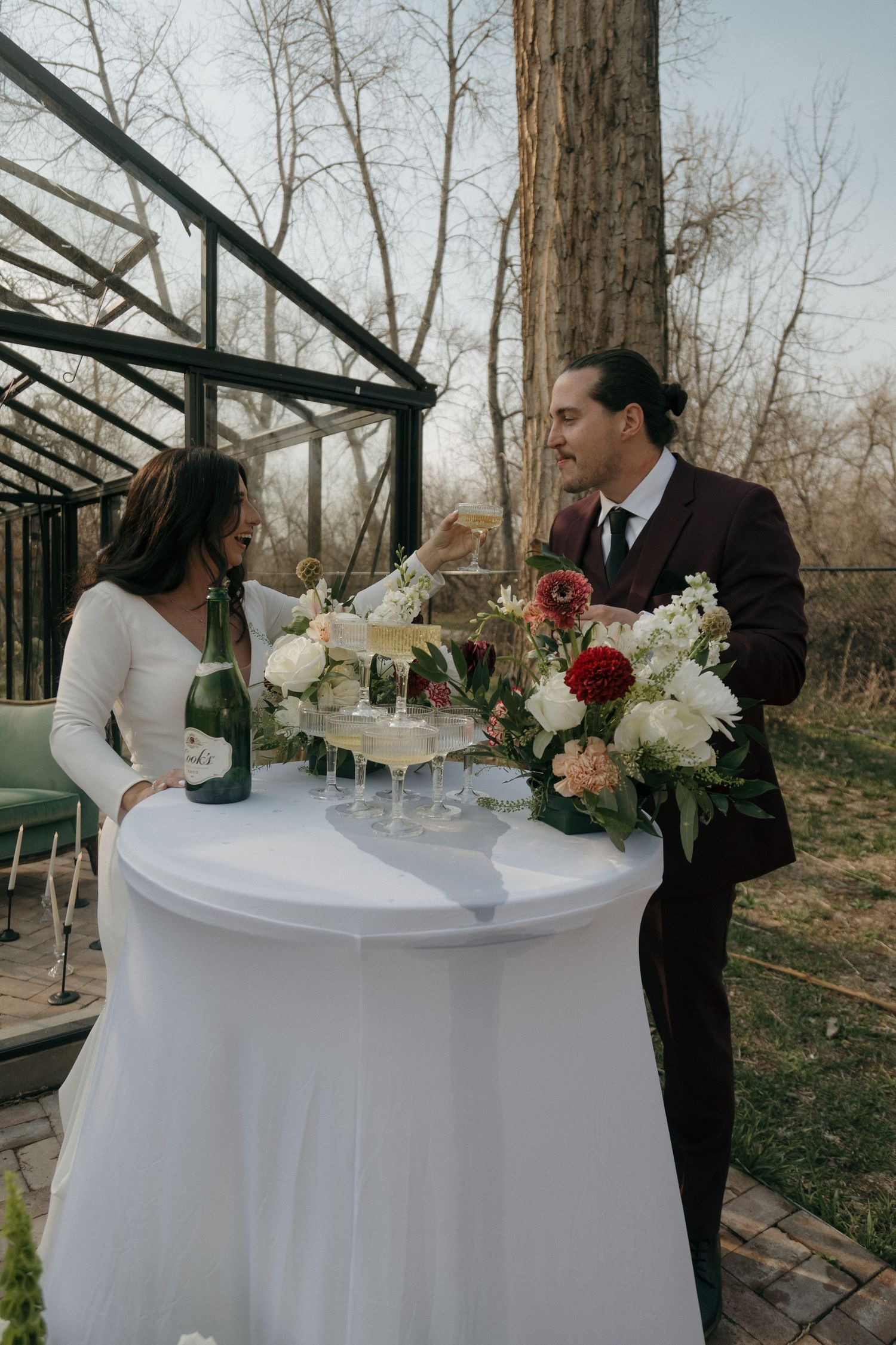 Bride and groom toast champagne at a floral decorated cocktail table at an outdoor wedding.