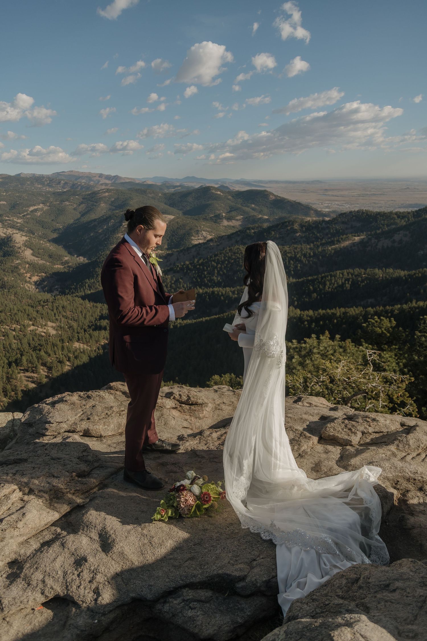 Officiant reads vows as bride and groom stand on dramatic rocky mountain overlook with panoramic valley views.