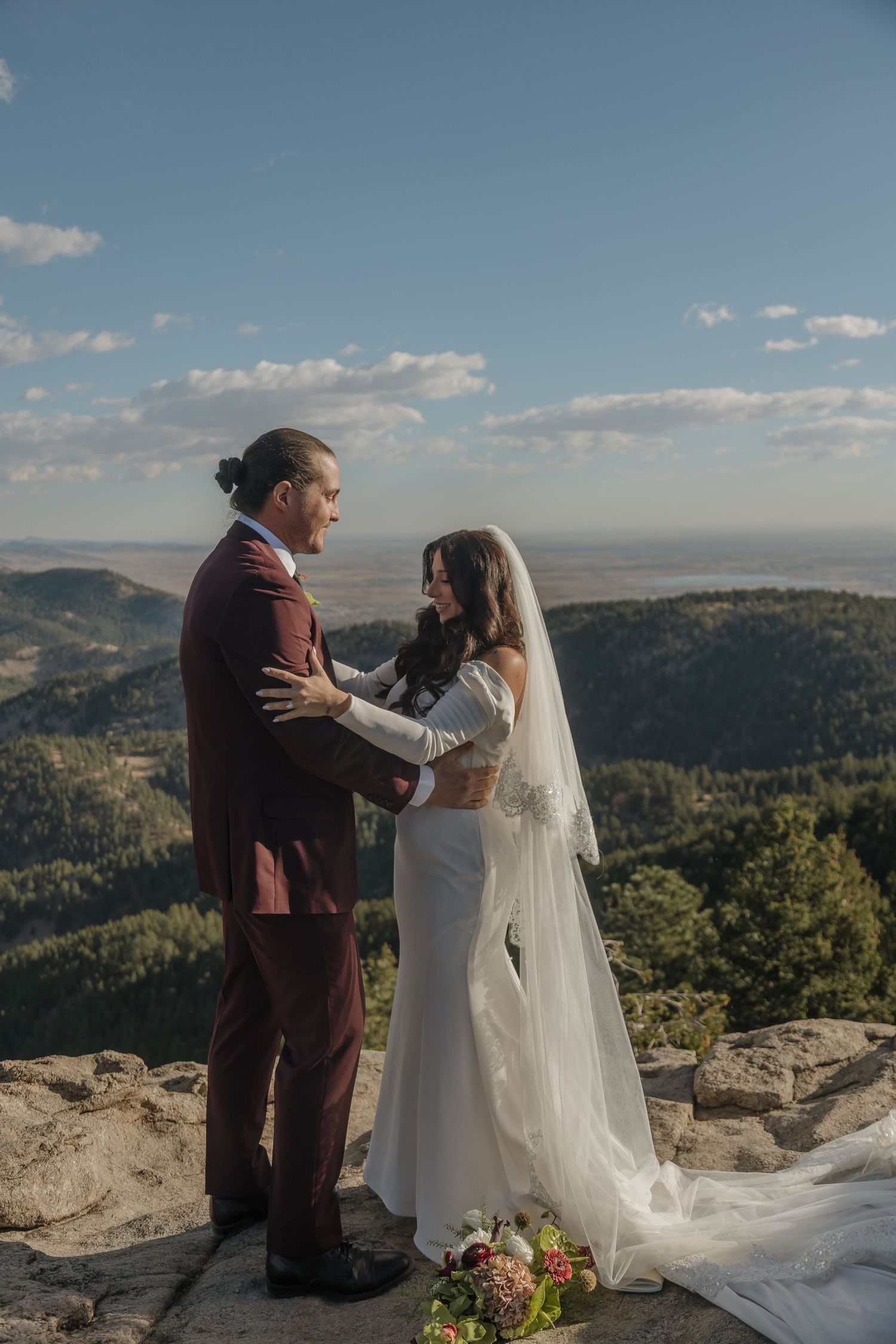 Bride and groom exchange vows on rocky mountain overlook with sweeping forest valley views.