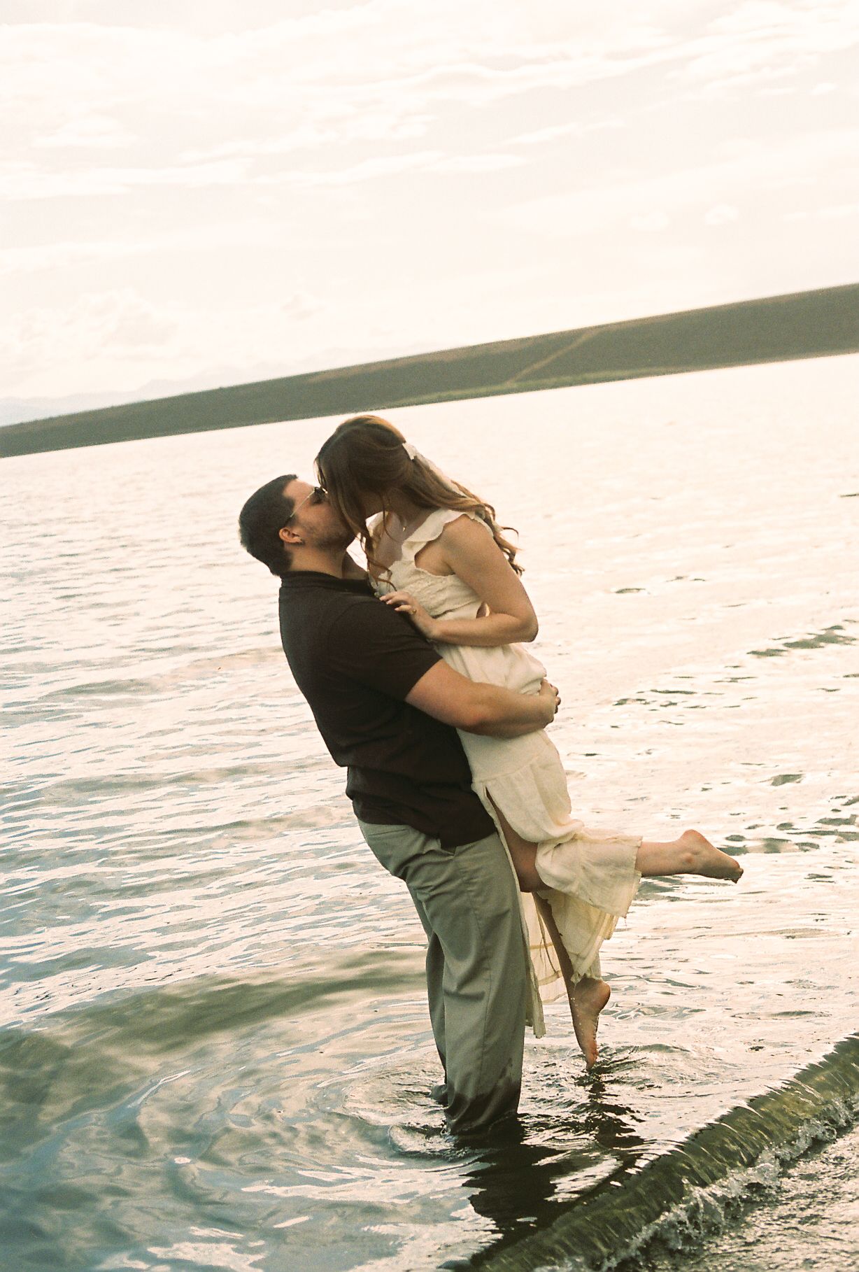Man lifting woman for a kiss while standing in a lake at sunset during an engagement shoot.