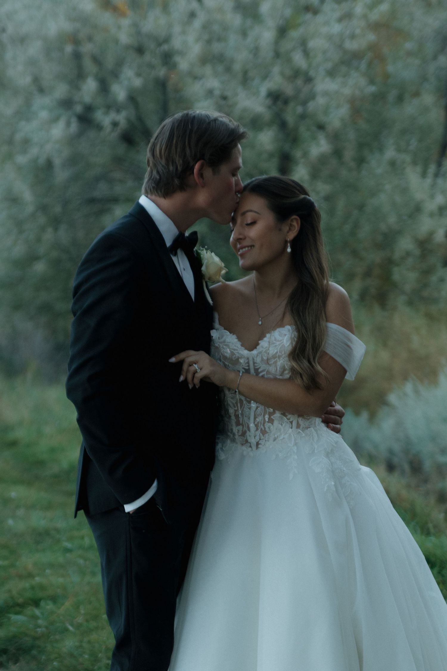 A tender moment between newlyweds against a backdrop of misty green trees.
