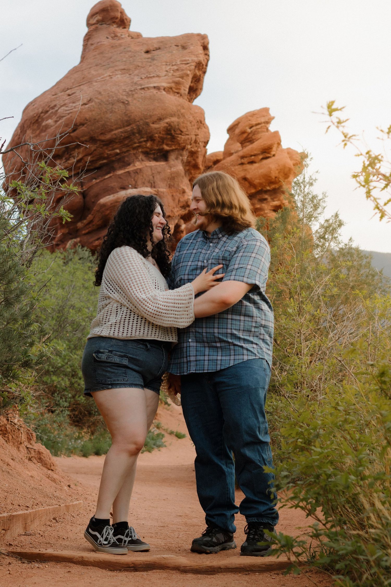 A couple shares a tender moment in front of dramatic red rock formations at sunset.