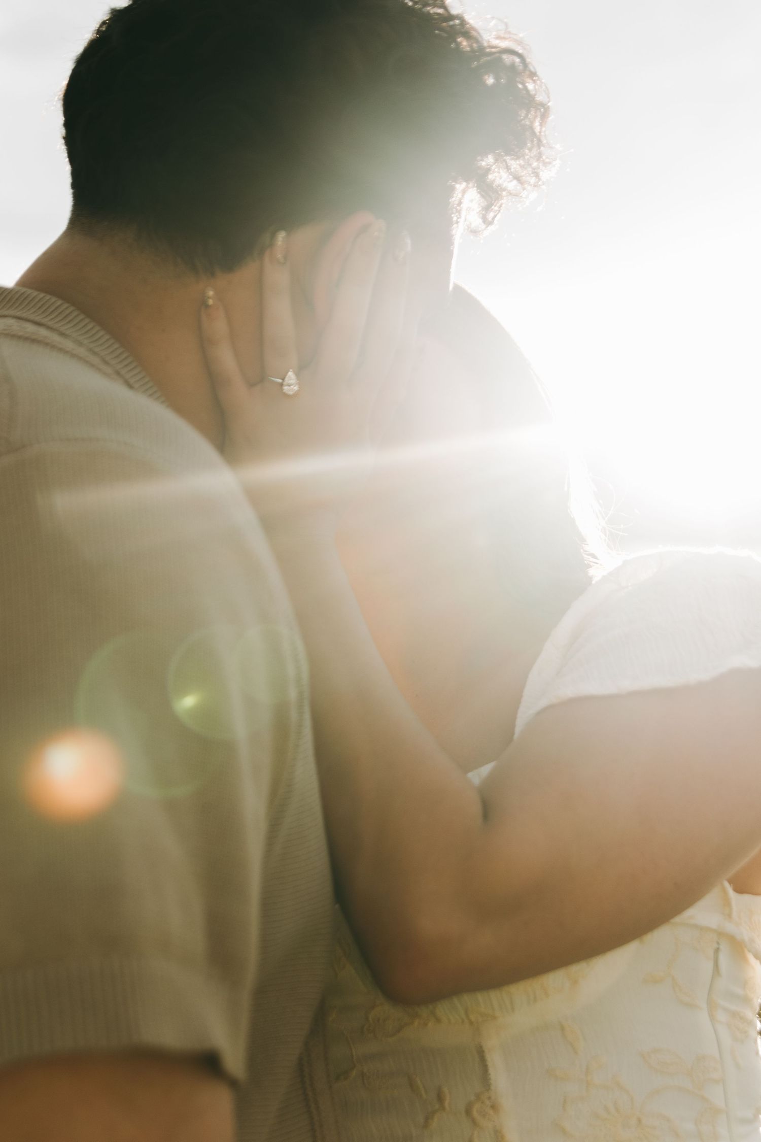 Intimate couple embraces in soft sunlit room with romantic lens flare creating dreamy atmosphere.