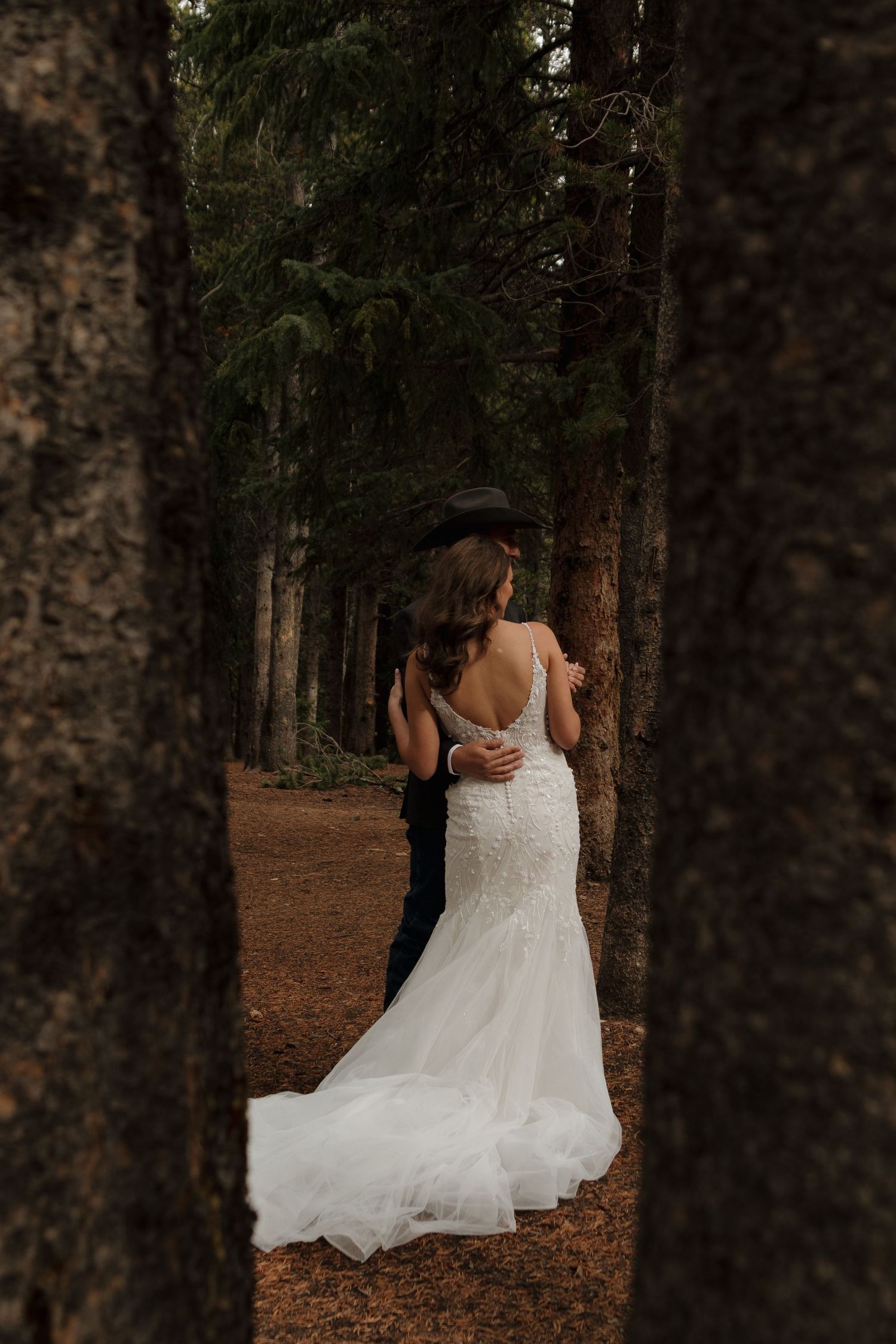 A couple shares an intimate moment among tall pine trees in a forest wedding setting.