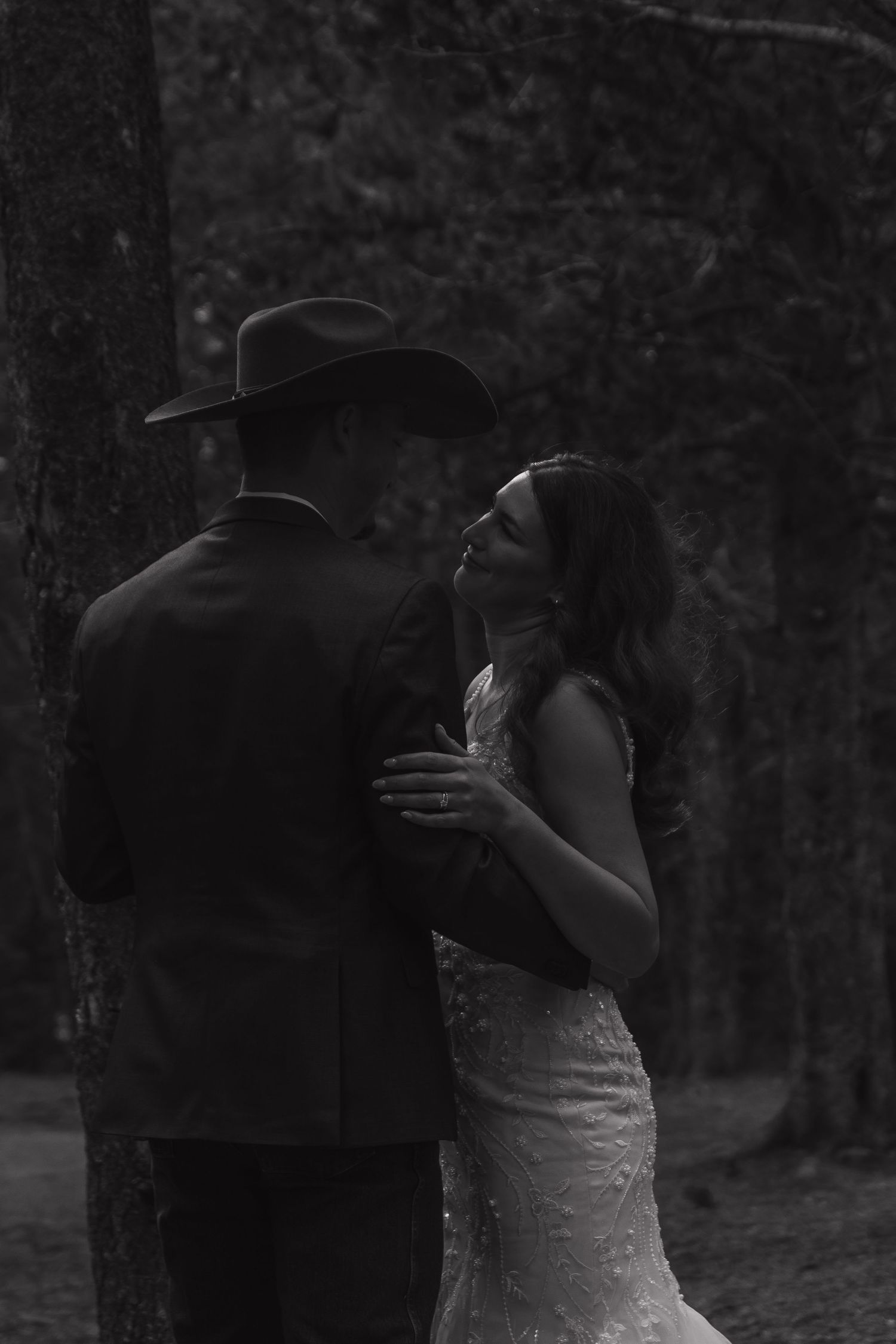 Intimate black and white wedding photo of a couple embracing in a forest setting.