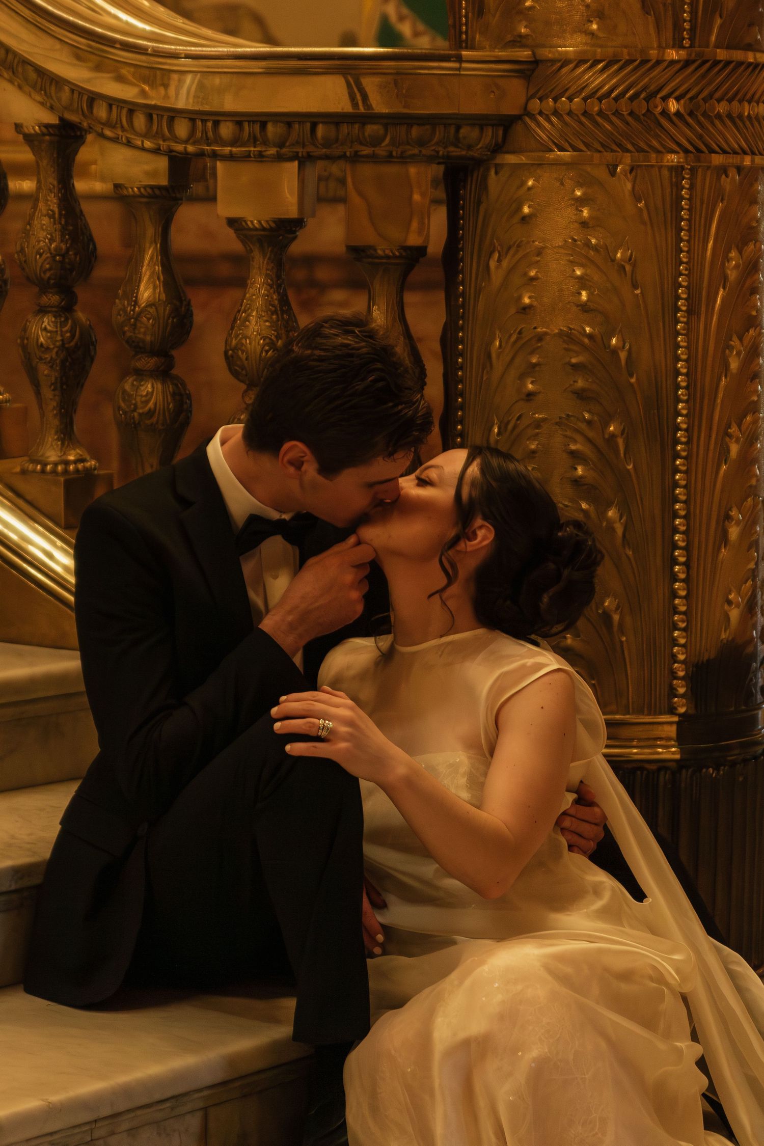 A romantic moment captured on an ornate staircase in warm golden lighting.