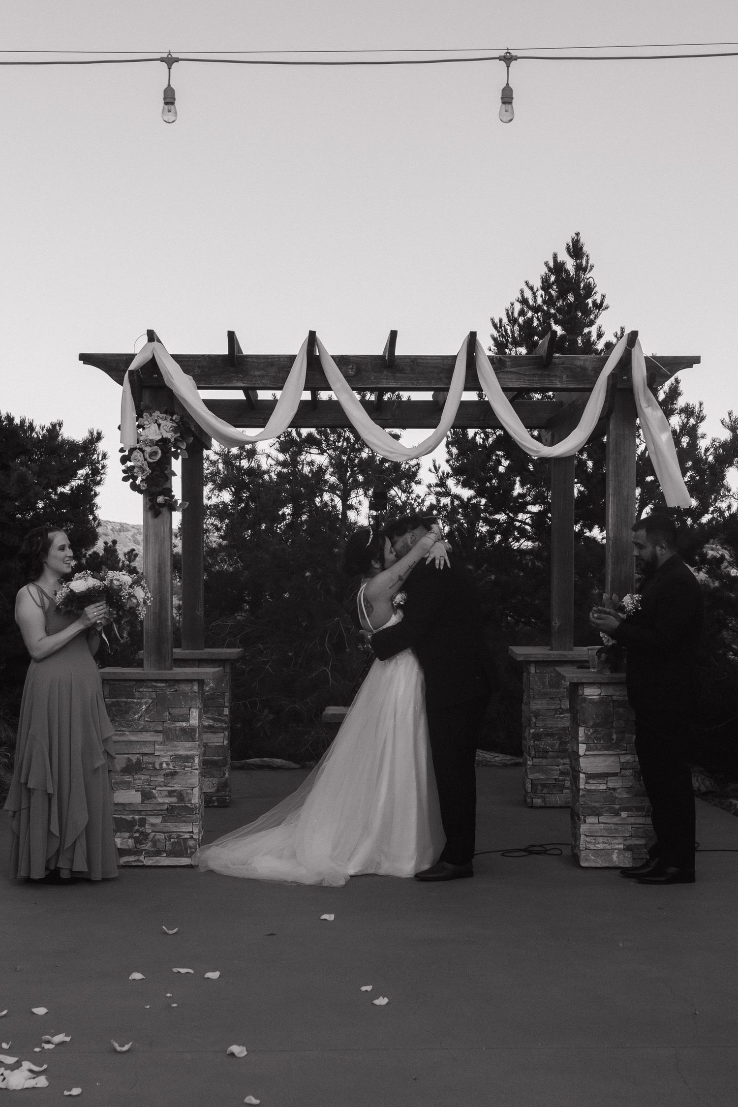 A black and white photo sequence shows a wedding ceremony progressing under a decorated pergola at dusk.