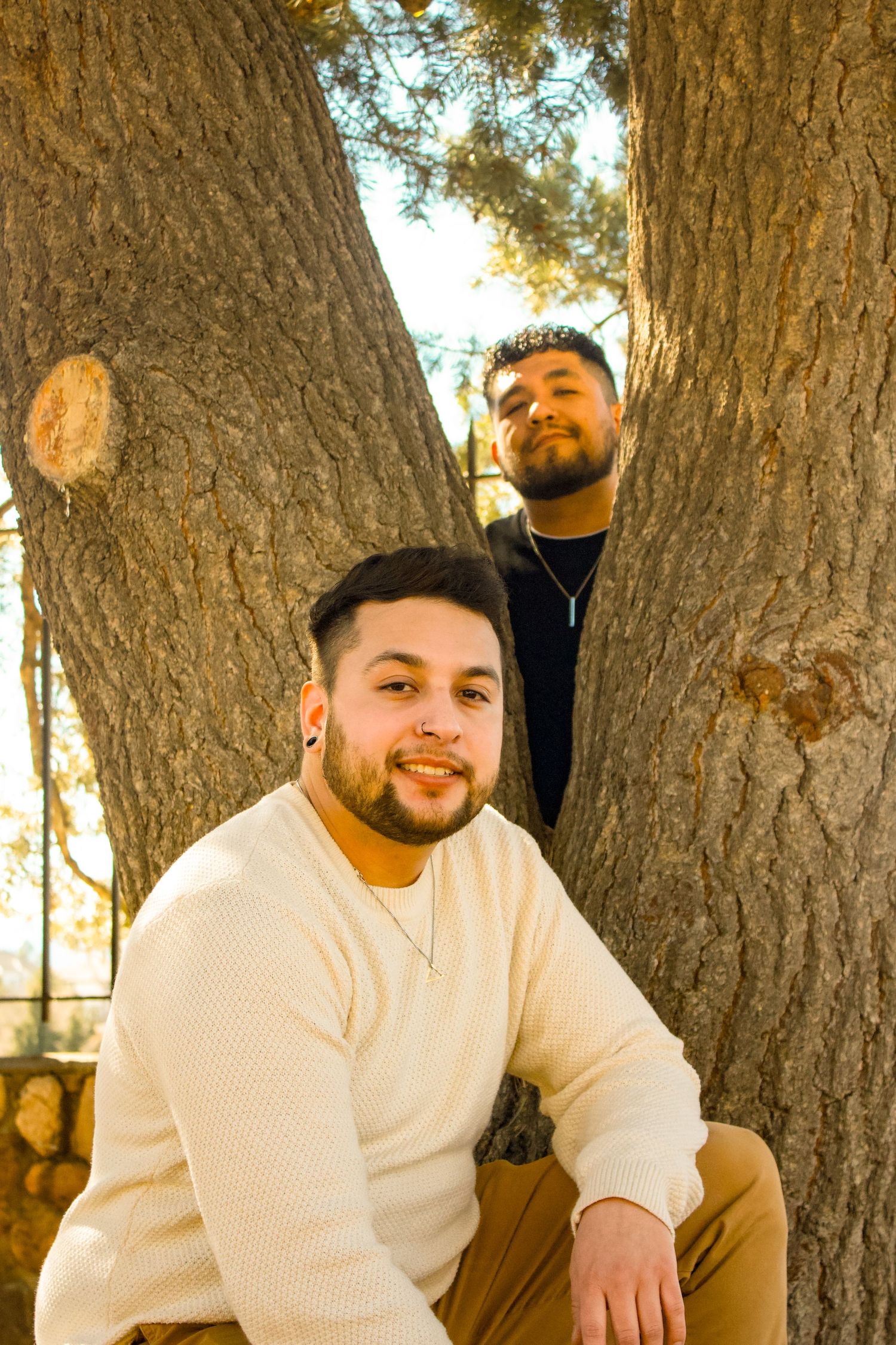 Two people posing between large tree trunks in warm sunlight during an outdoor photoshoot.