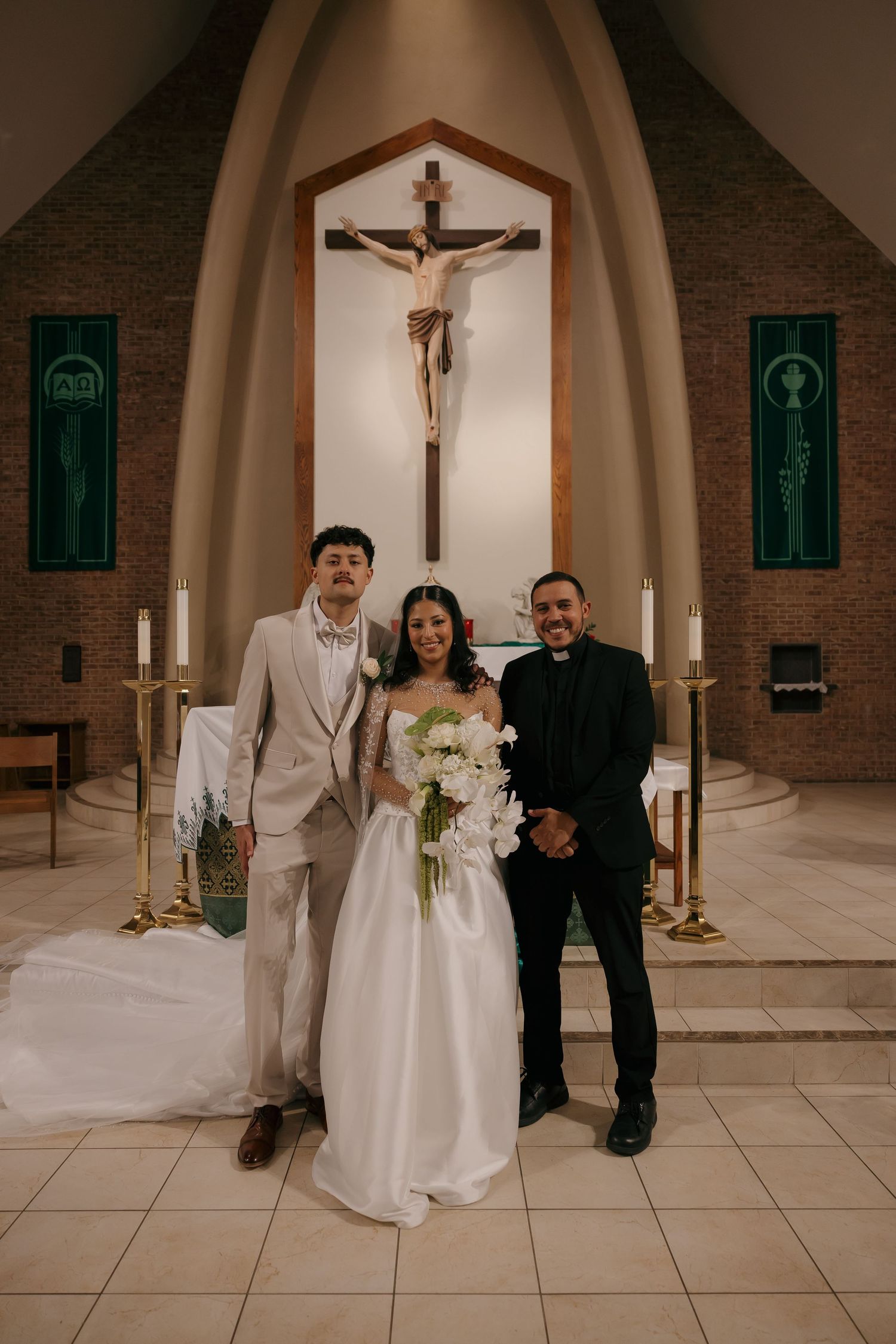 Bride and groom pose with priest at church altar after Catholic wedding ceremony.