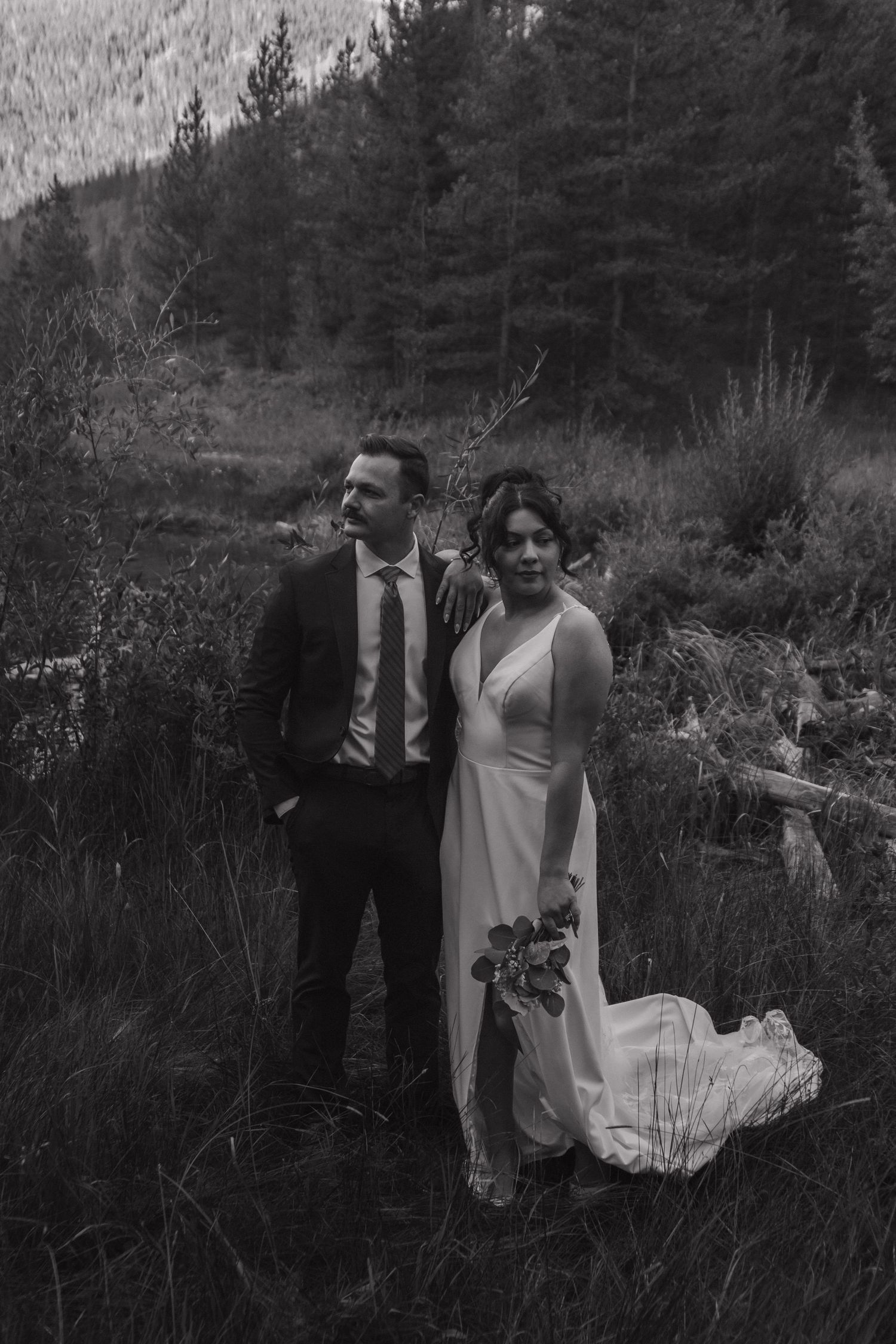 An intimate outdoor wedding ceremony set against a backdrop of evergreen forest in black and white.