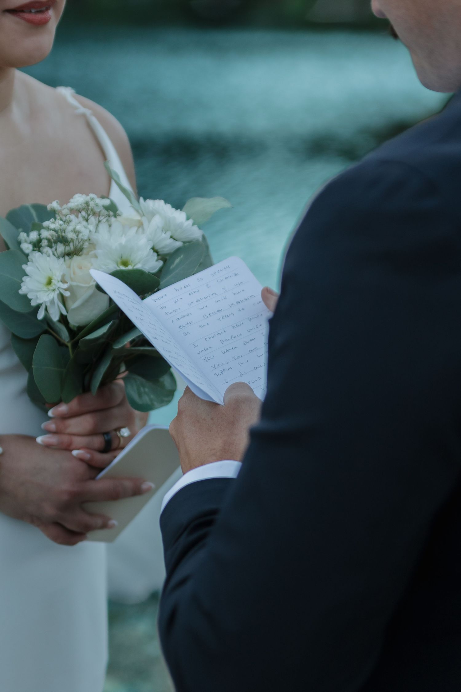 A couple holding white flowers and handwritten notes during an intimate outdoor wedding ceremony.