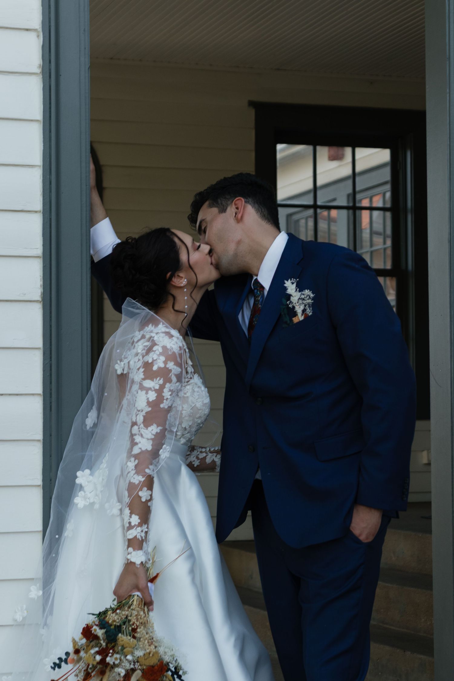 Romantic moment between newlyweds under a white building's archway.