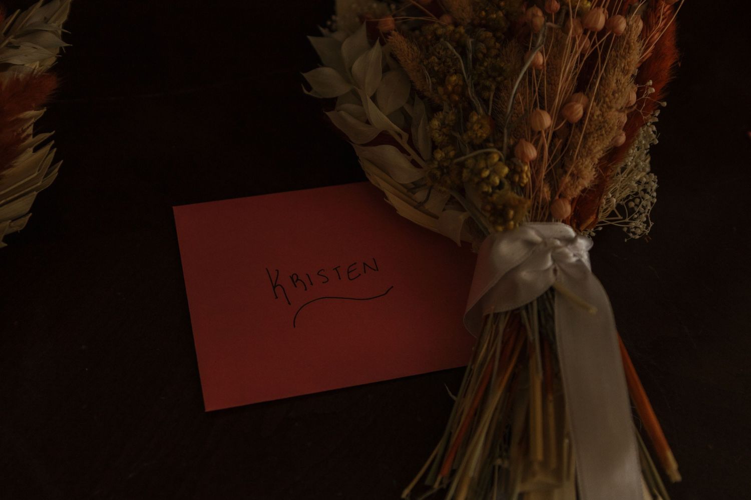 Multiple dried flower arrangements with white ribbon bows arranged in a moody, dark setting.