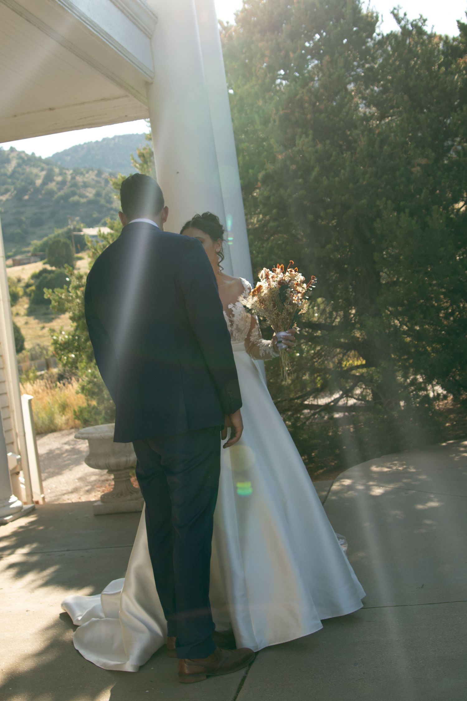 Wedding couple in formal attire walking on white portico with mountain views.