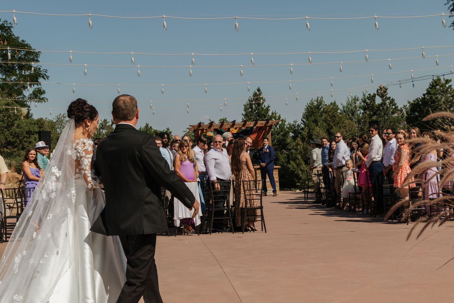 Wedding ceremony outdoors with string lights overhead and guests seated in rows.