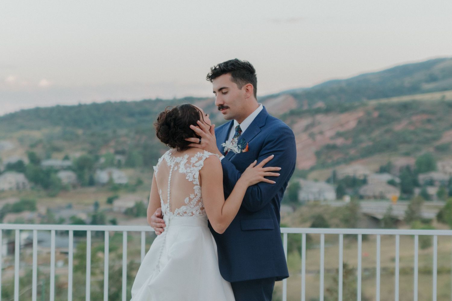 Couple shares an intimate moment on a balcony with mountain scenery behind them.