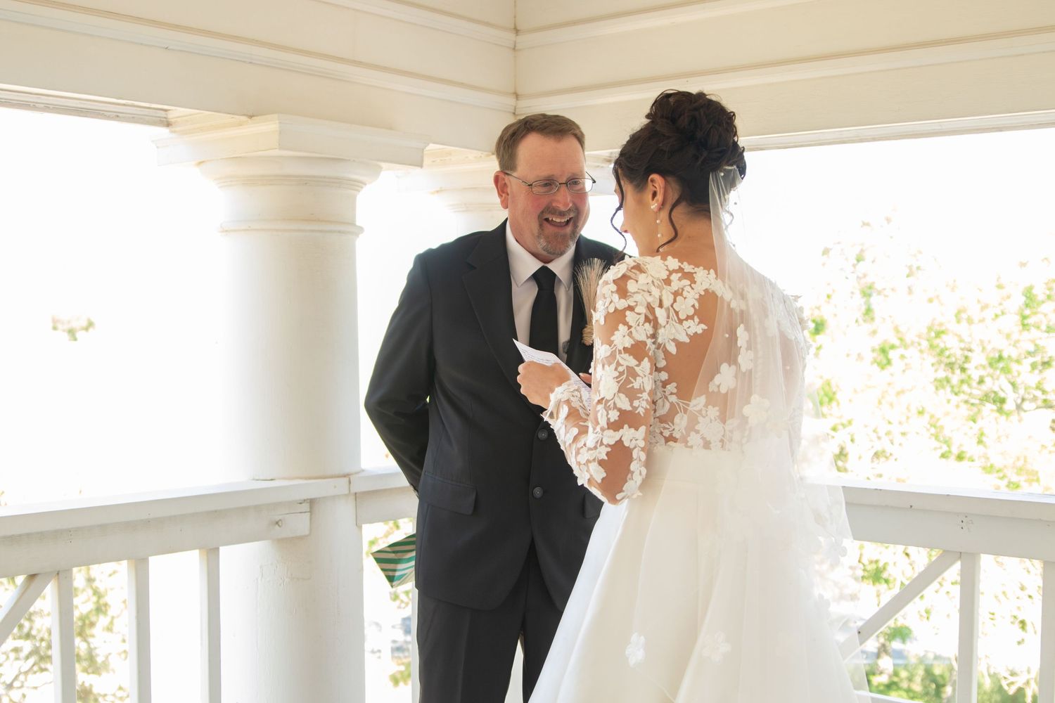 Couple shares intimate moment during first look on a bright white porch.