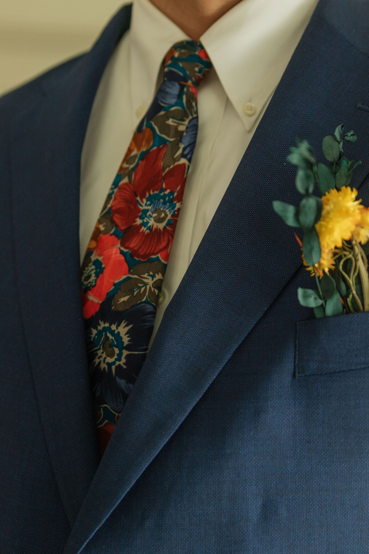Close-up of navy blue suit jacket with floral tie and yellow boutonniere.