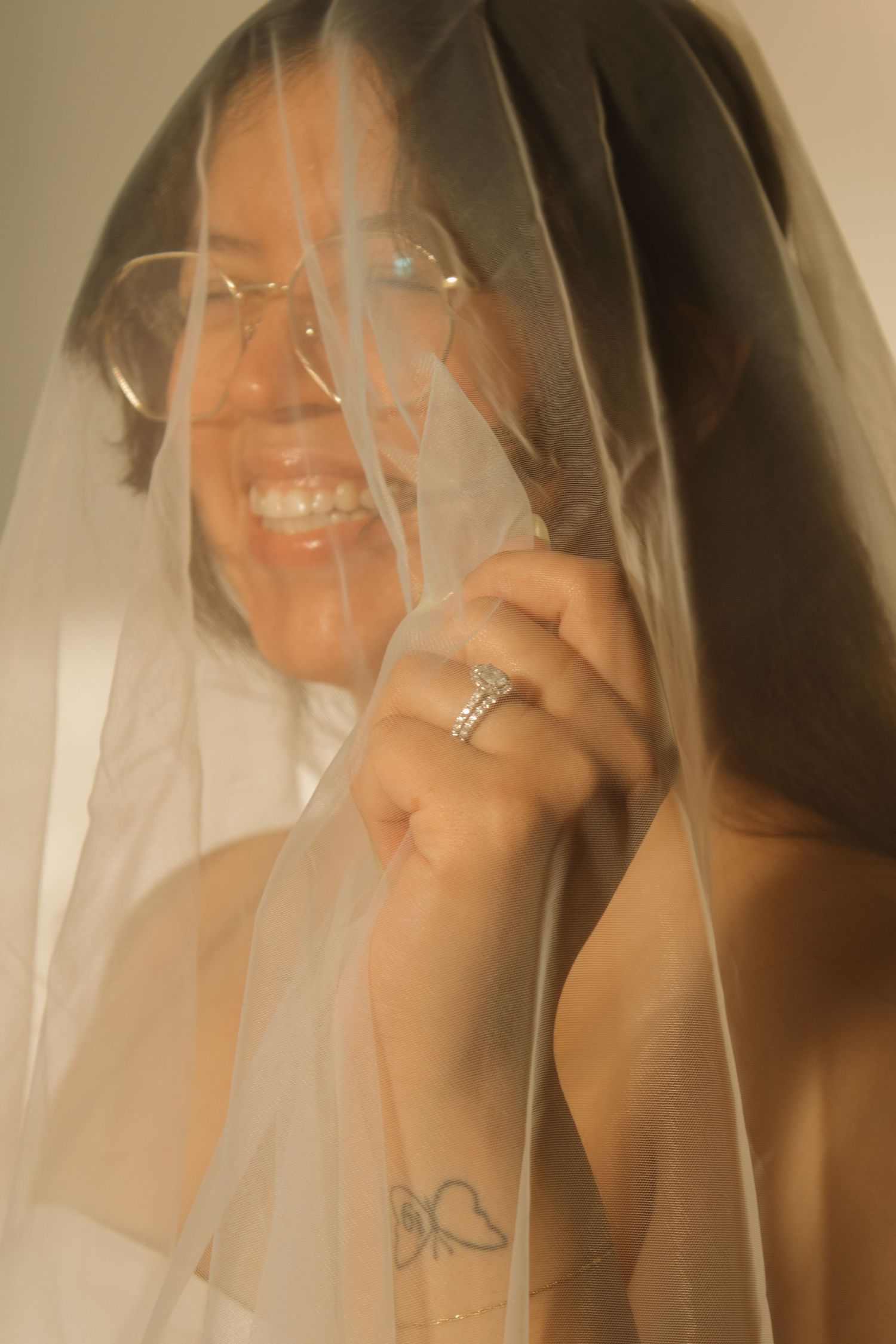 A joyful moment captured through a delicate bridal veil showing an engagement ring.