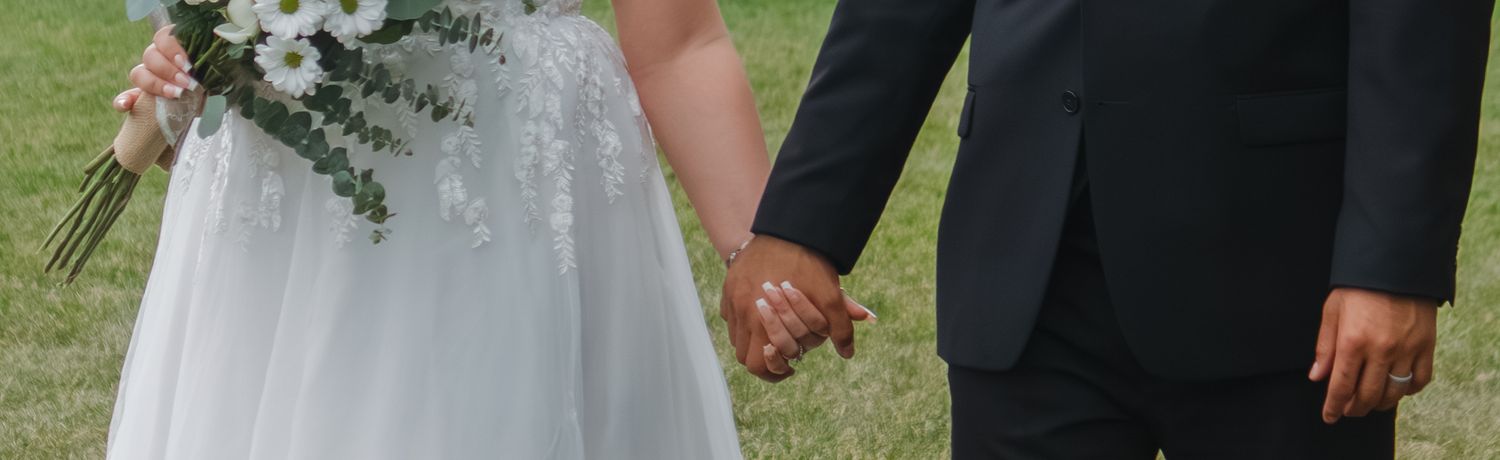 Wedding party stands together outdoors holding floral bouquets and wearing formal attire.