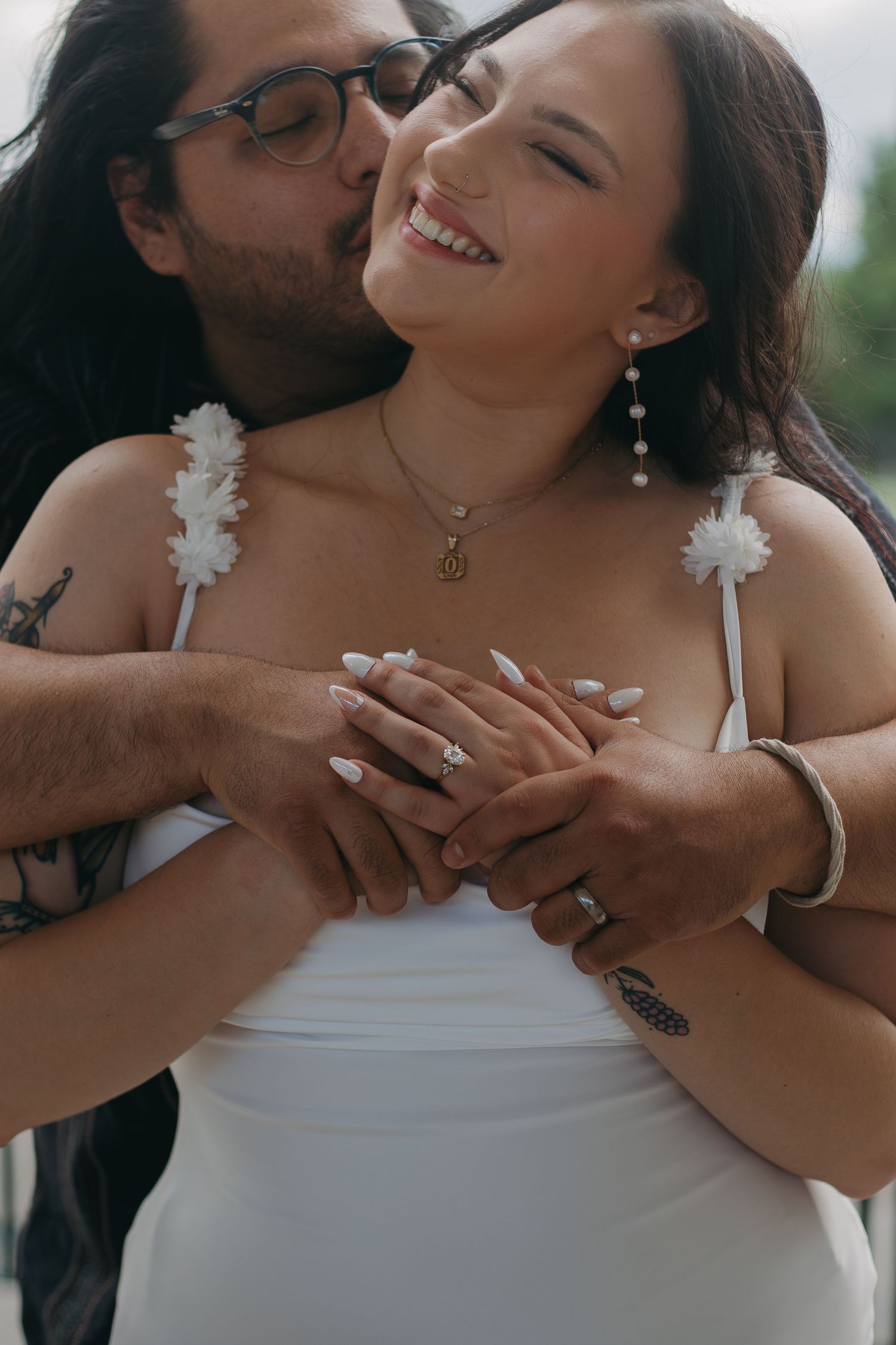 Close-up of a tender wedding moment showing embracing couple with bride in white dress and floral strap details.