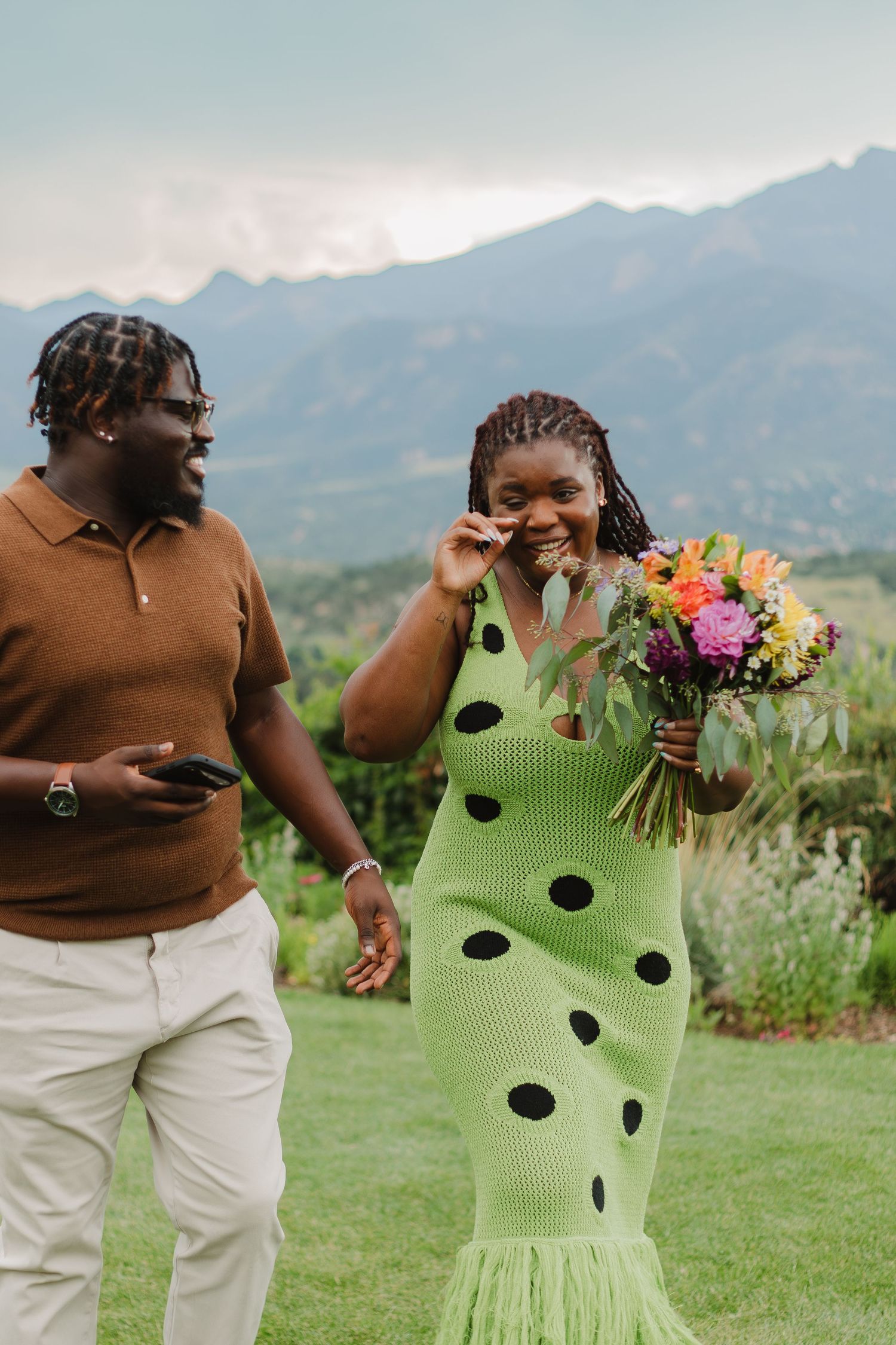 A couple shares a joyful moment in front of mountain scenery while holding a colorful bouquet.