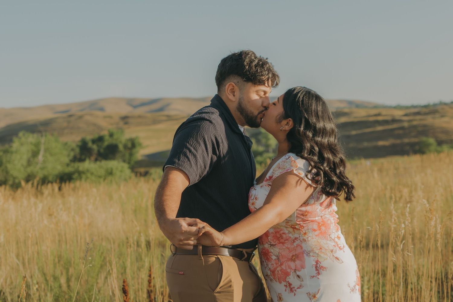 A couple dances together in a field with mountains visible in the distance.