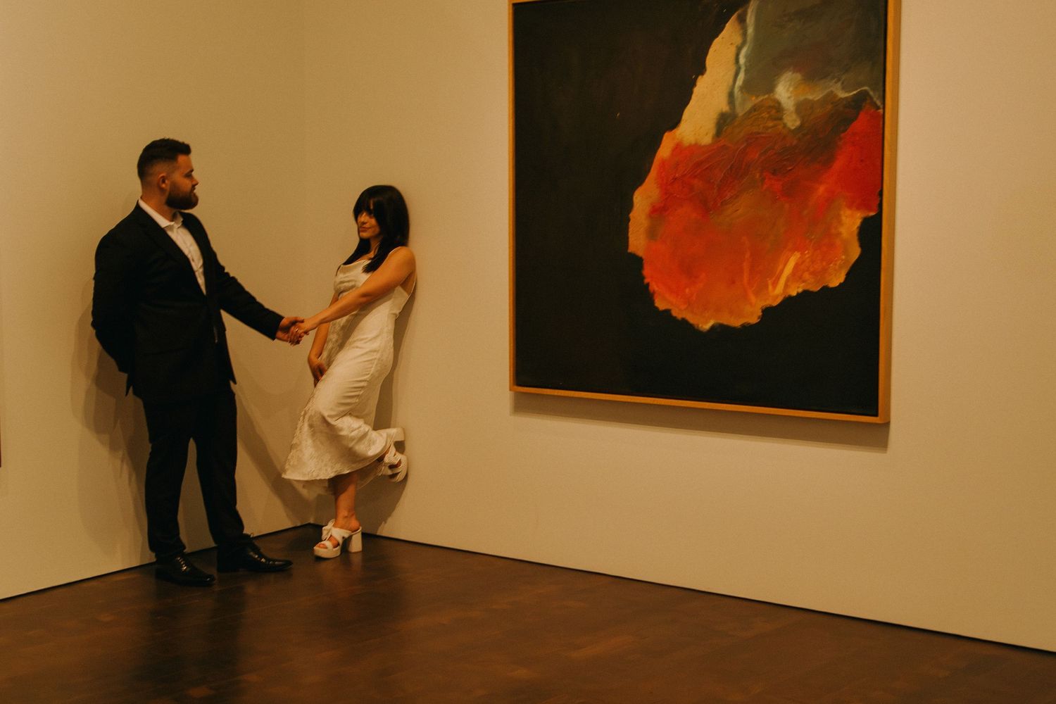 A couple dances playfully in front of a vibrant abstract painting in an art gallery.
