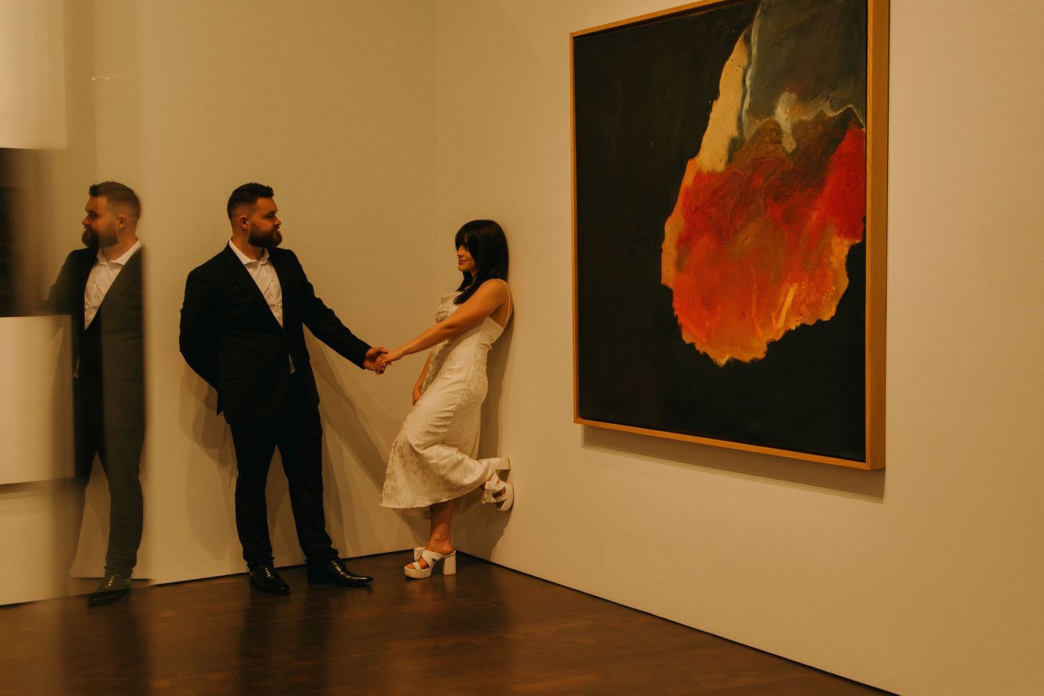 Art gallery interior showing white walls with paintings and people viewing artwork in a modern space.