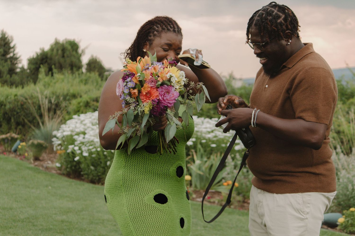 A couple examines a colorful bouquet of flowers in a garden with mountains visible behind.