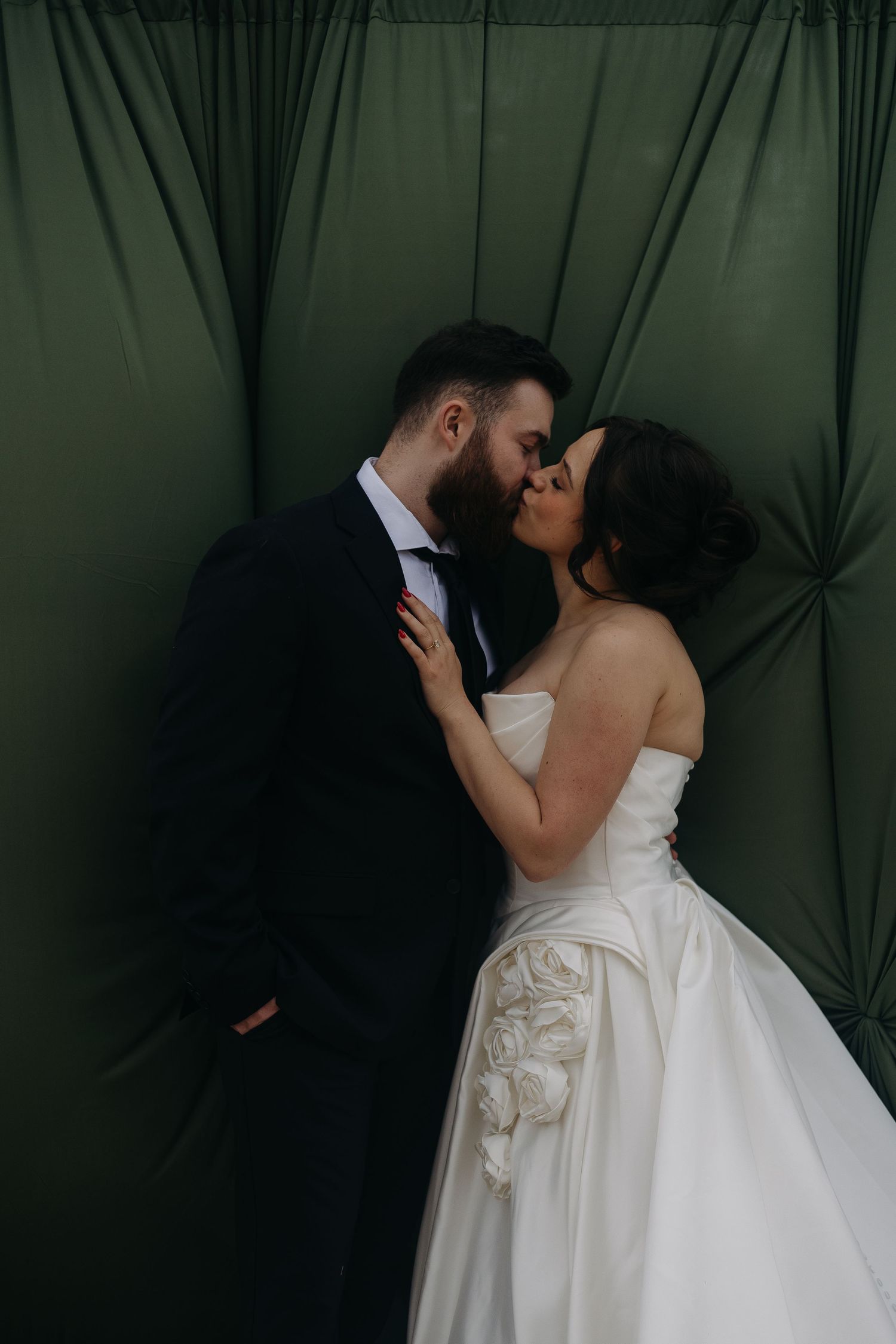 A romantic wedding portrait of a couple sharing an intimate moment against a dark green draped backdrop.
