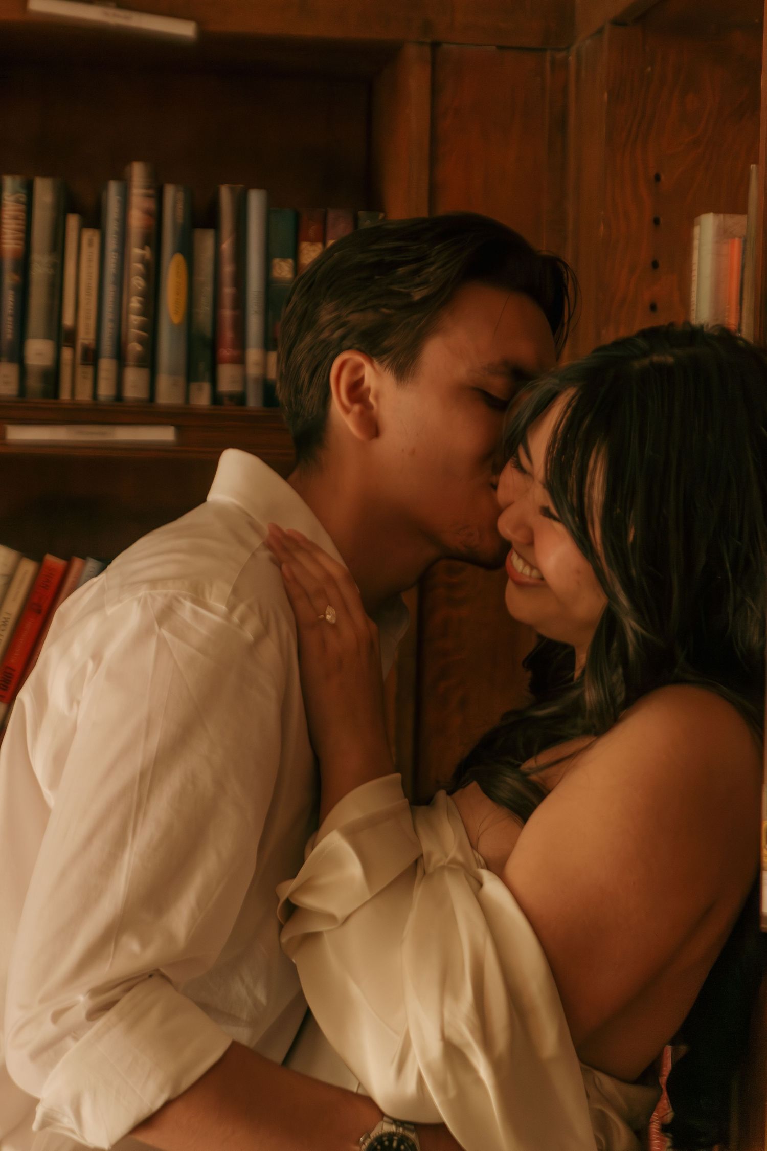 An intimate moment shared between two people in a library setting with wooden bookshelves in the background.