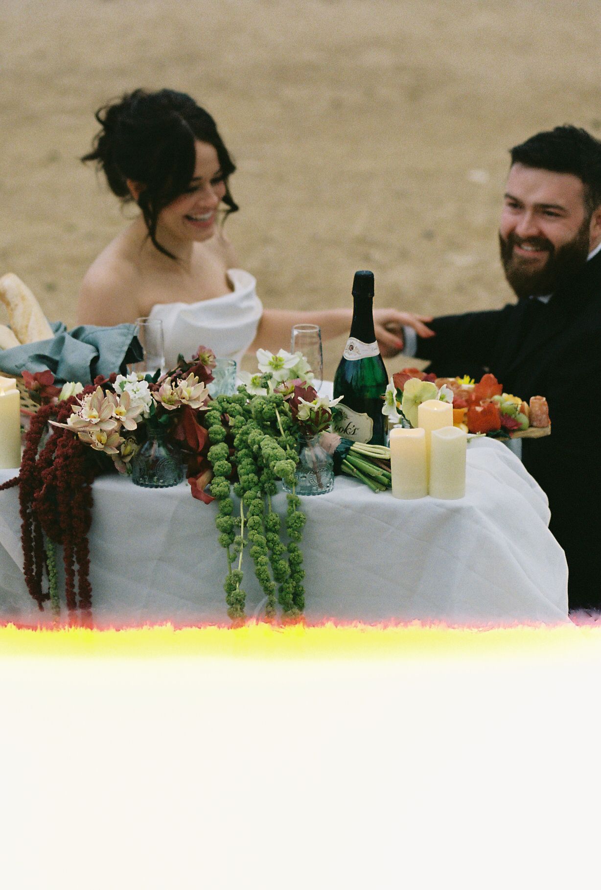 A wedding table setting with champagne, flowers, and candles against a natural backdrop.