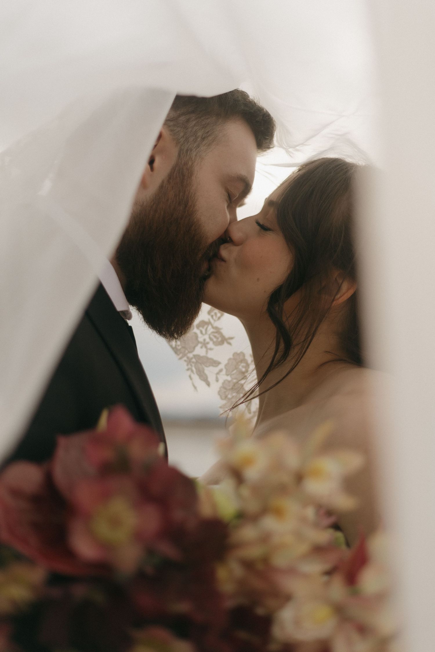 Romantic moment captured through sheer fabric with burgundy flowers in foreground.