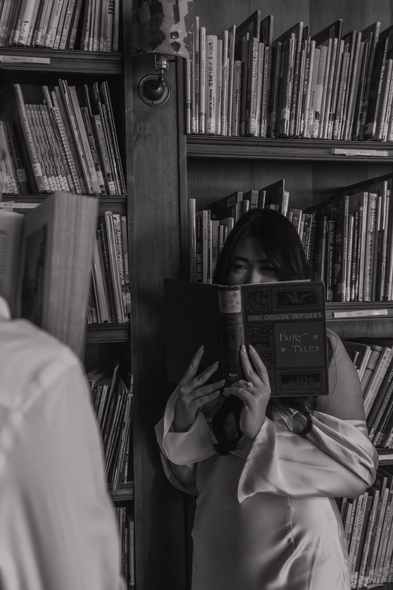 Black and white sequence showing a person hiding behind books on a library shelf.