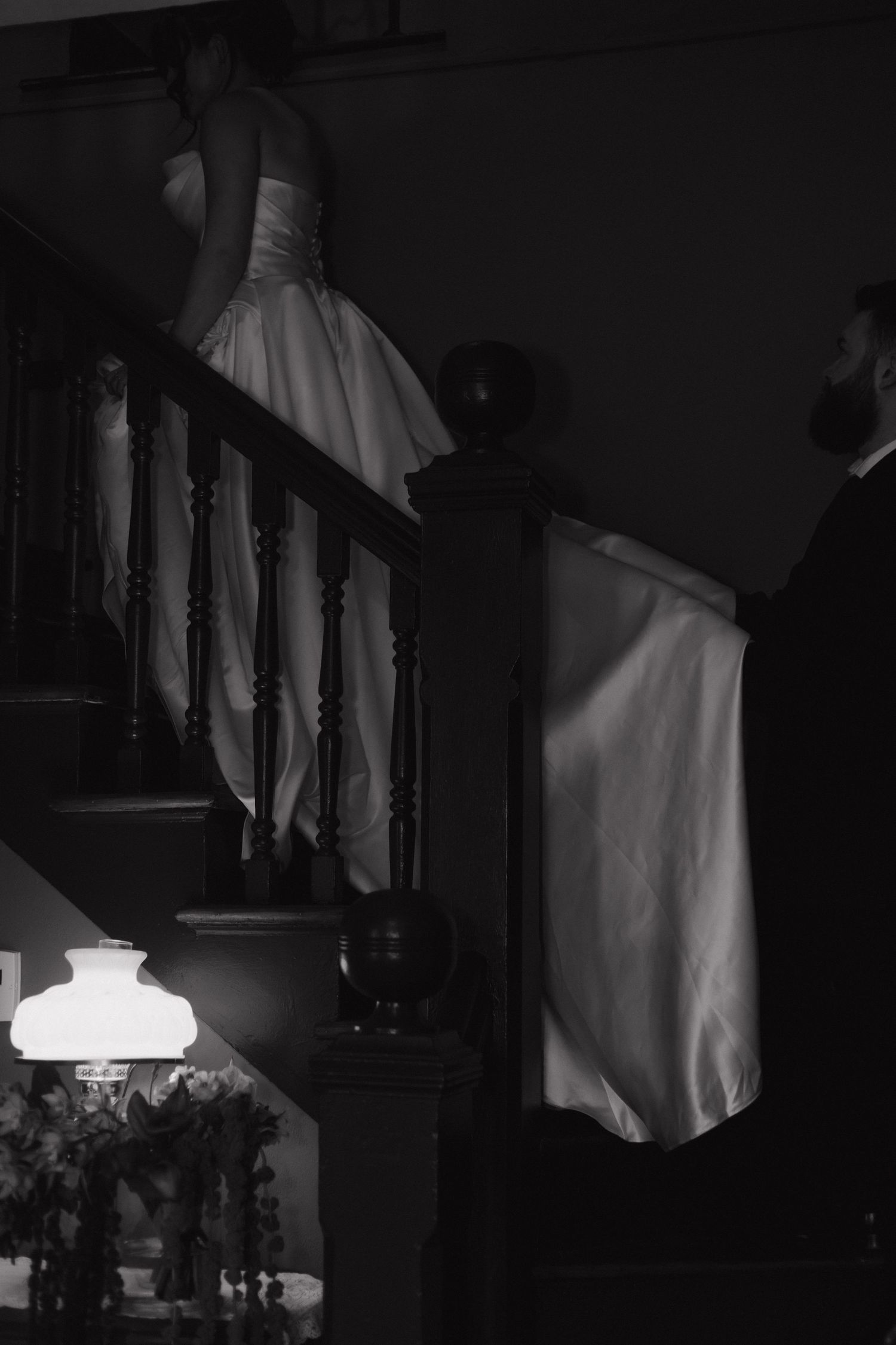 Dramatic black and white silhouette of a wedding dress on stairs with ambient lighting.