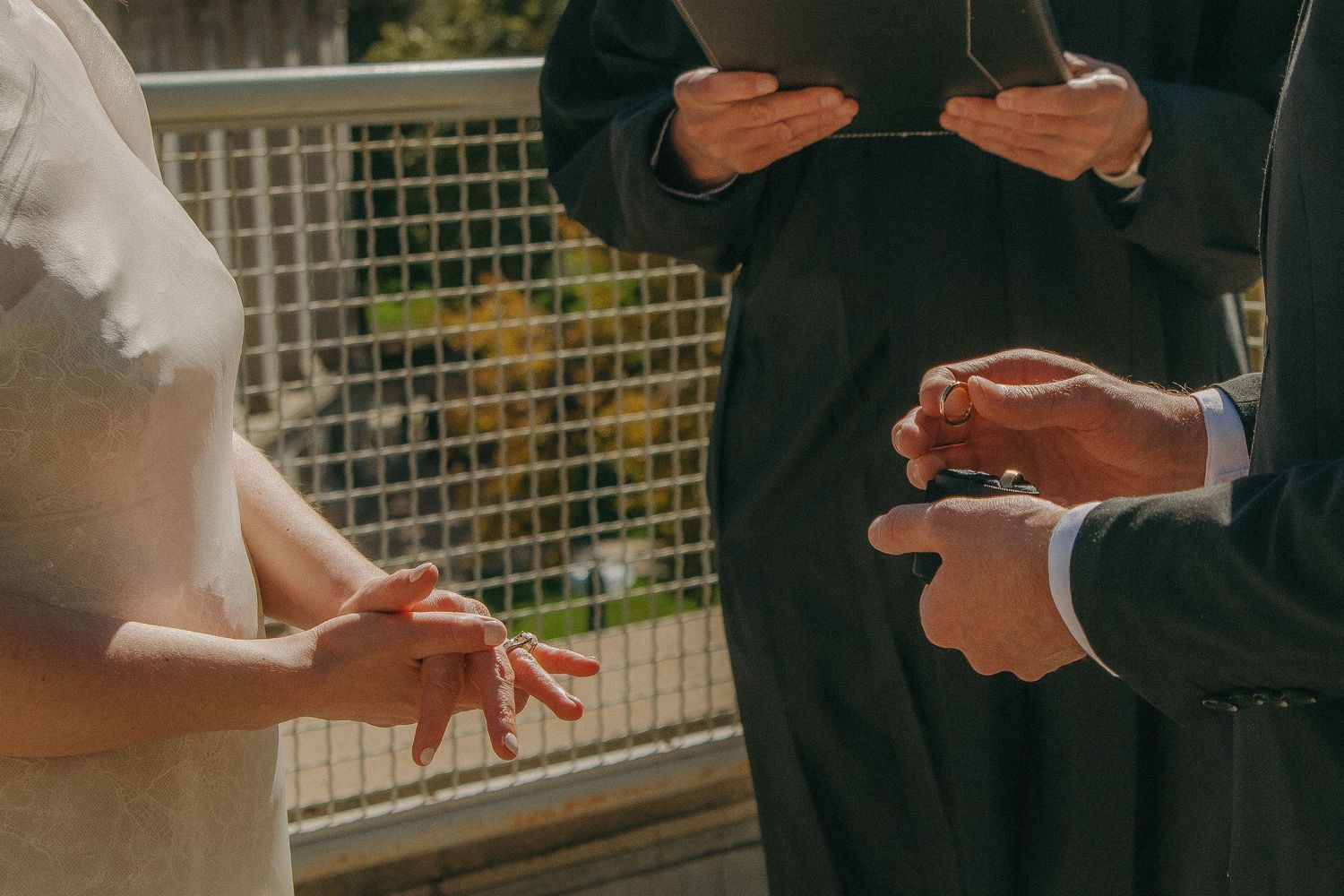 Close-up of hands during a wedding ring exchange ceremony outdoors.