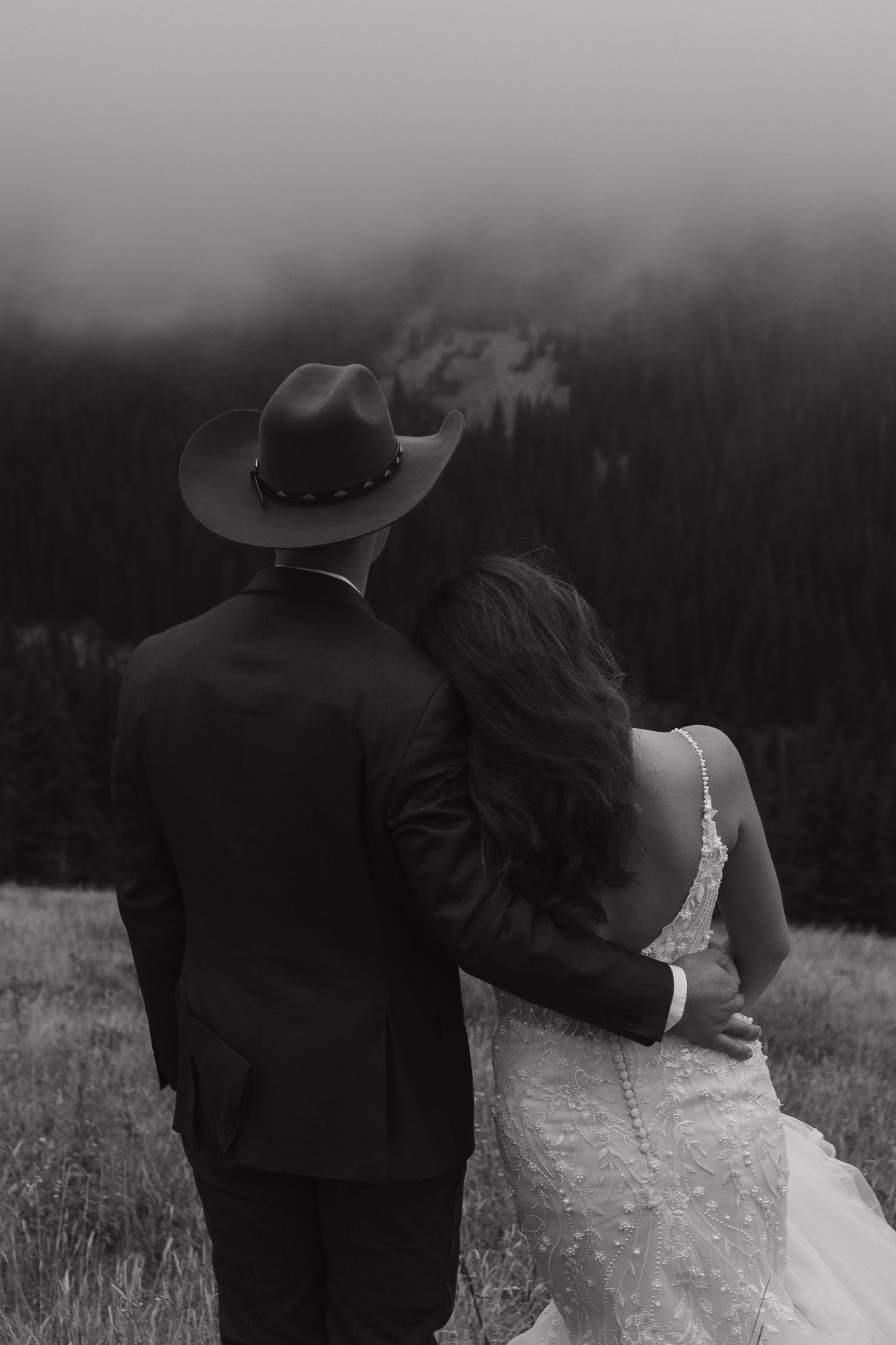 A black and white photo of a couple embracing while looking out over a misty mountain landscape.
