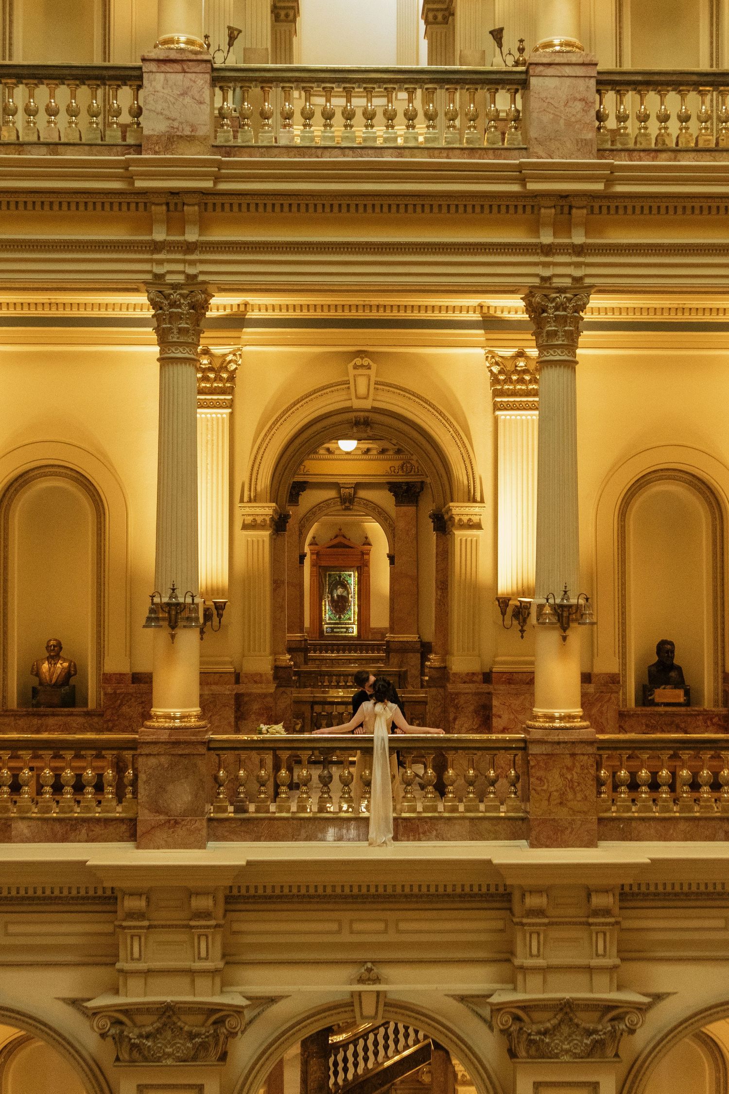 Ornate interior balcony with golden lighting showcases classical architectural details and columns in a grand historic building.