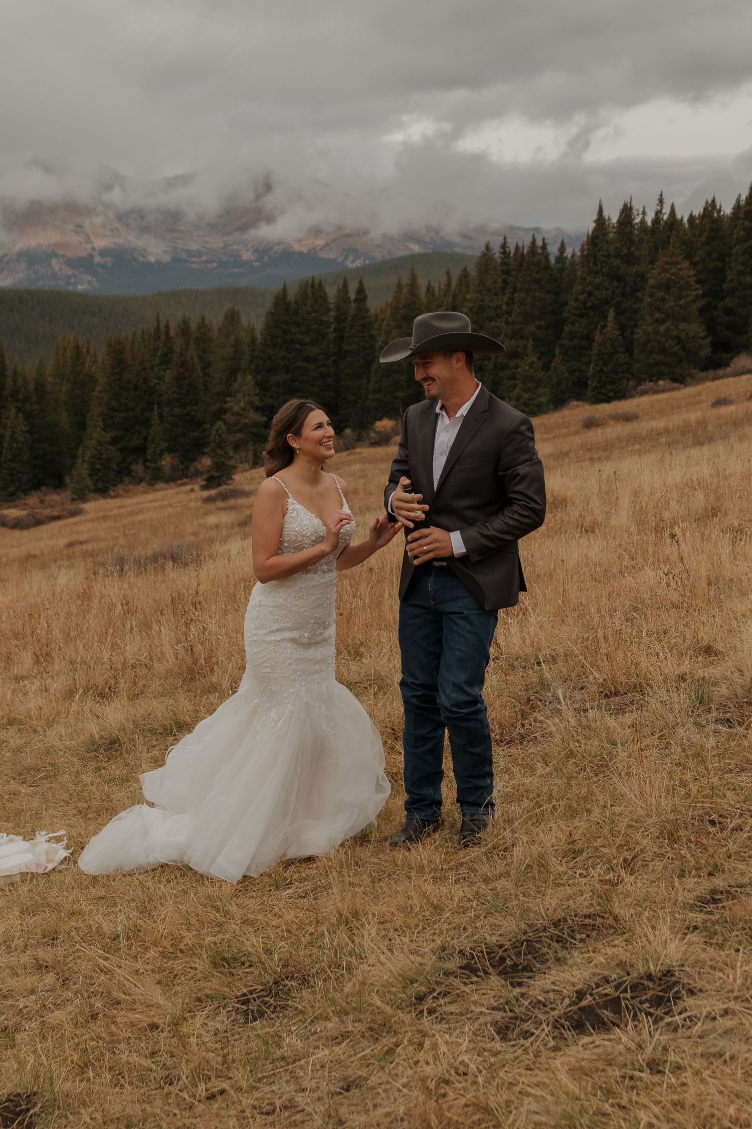 Wedding couple shares a moment on a mountainside meadow with evergreen forests in the background.