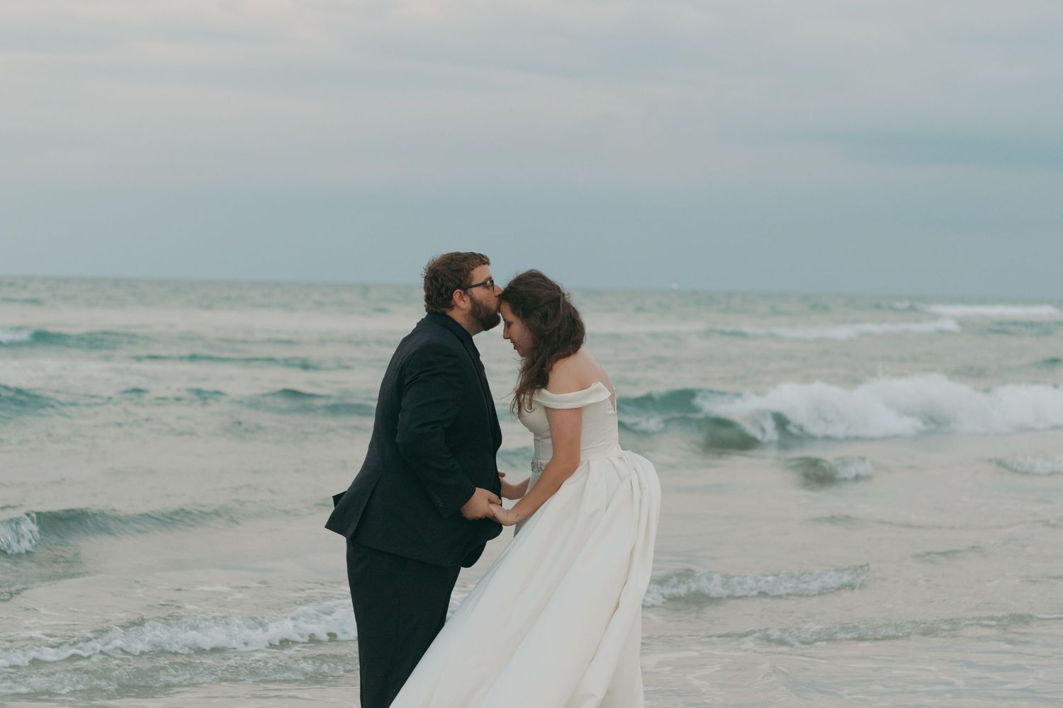 A couple shares a romantic moment on a misty beach with crashing waves in the background.