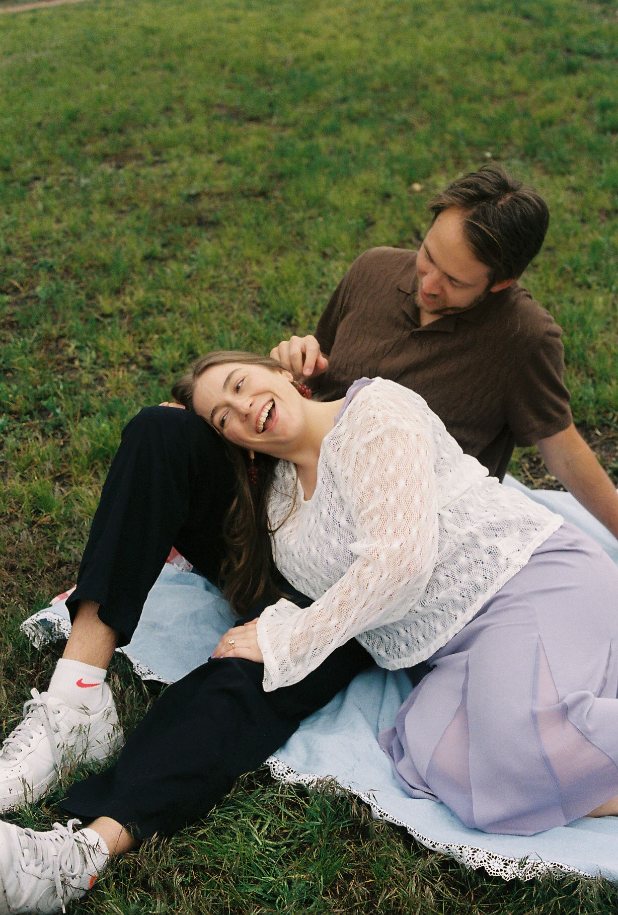 Joyful couple playing and laughing together on a picnic blanket in a green grassy park.