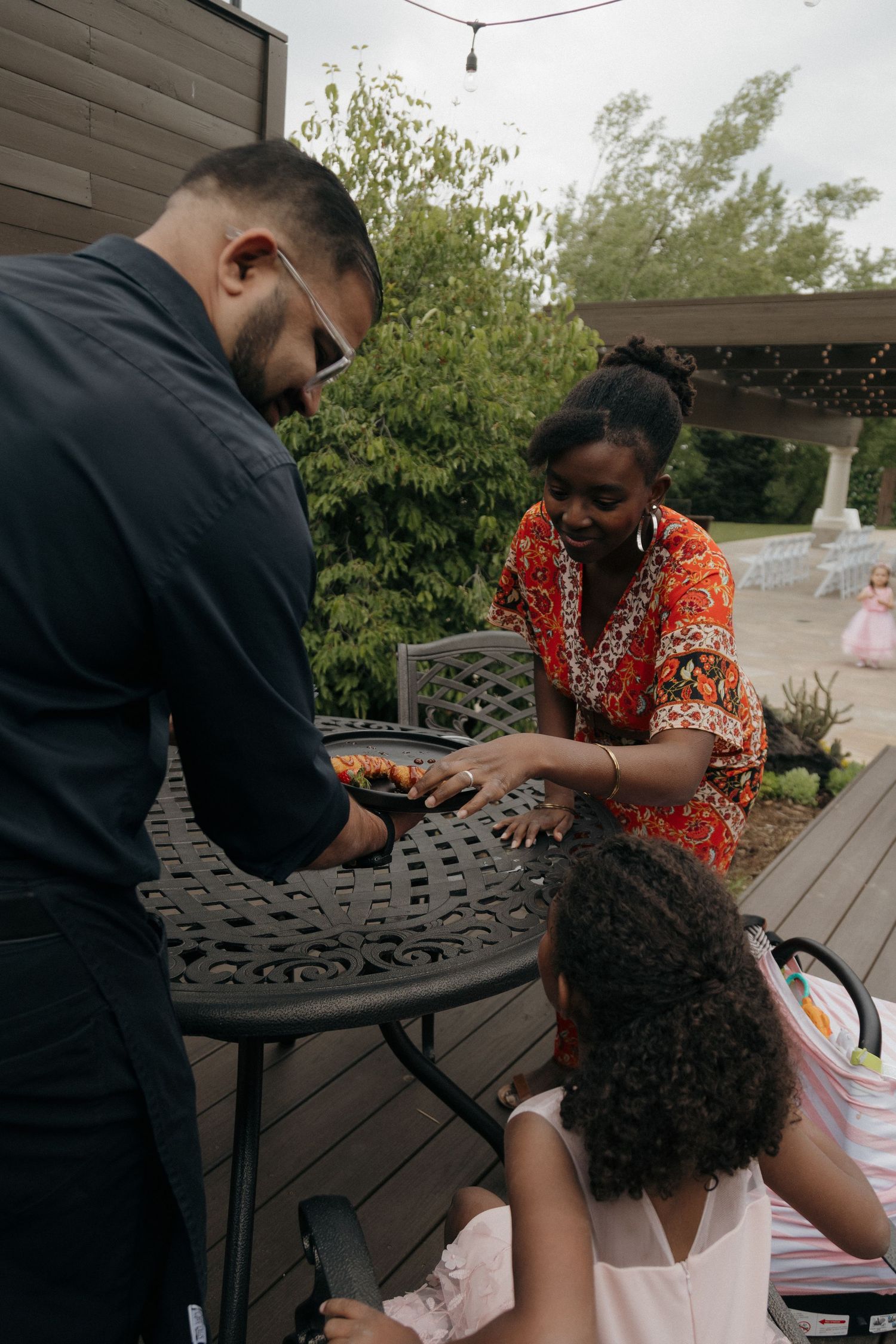 Catering staff serves food to guests at outdoor wedding reception on wooden deck.