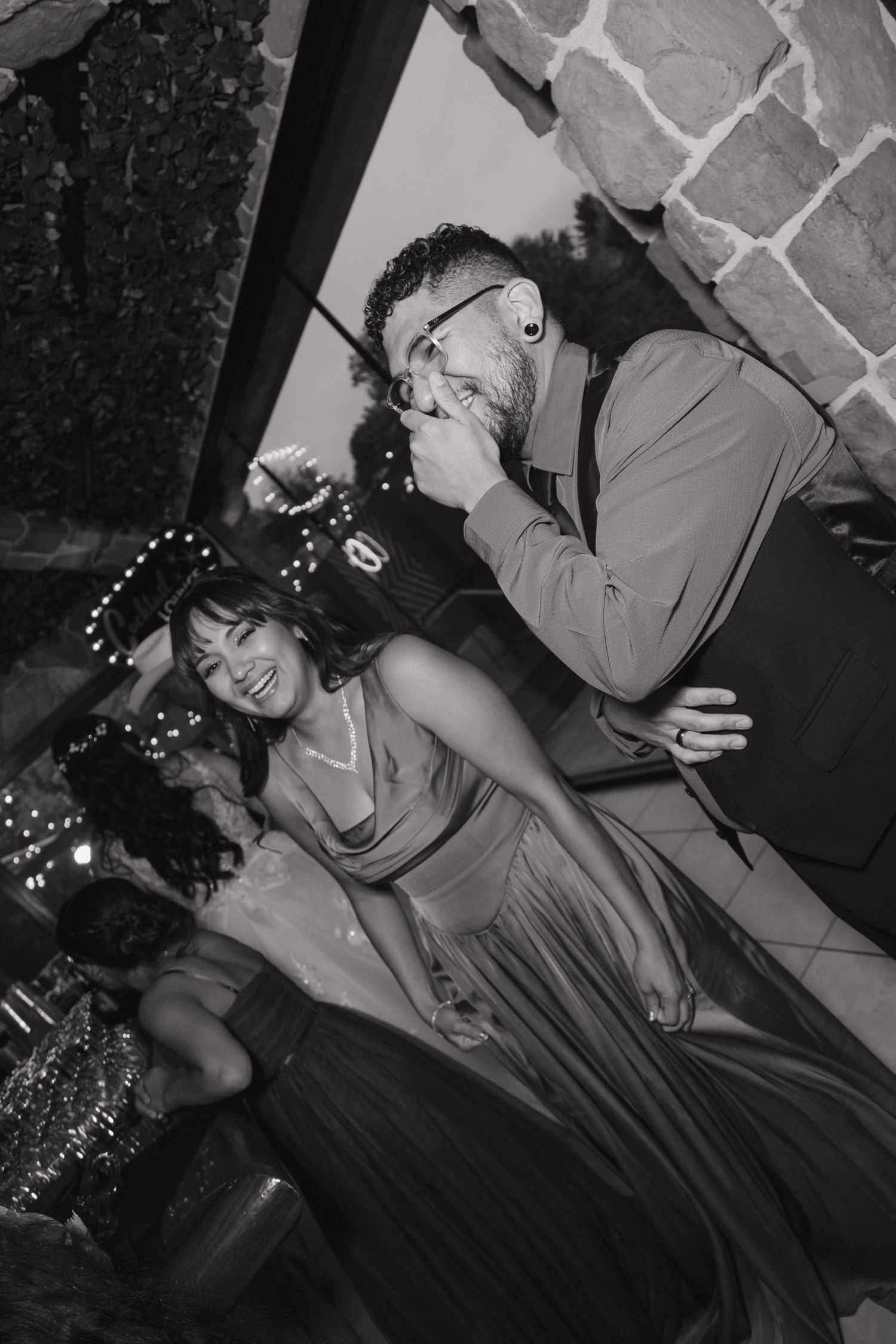 Man and woman laugh together at lively wedding reception in black and white candid photo.