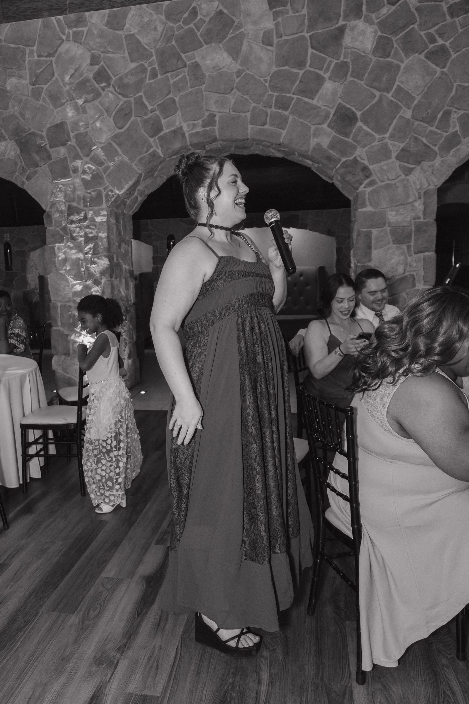 Wedding guest sings into a microphone on the dance floor in a black and white reception photo.